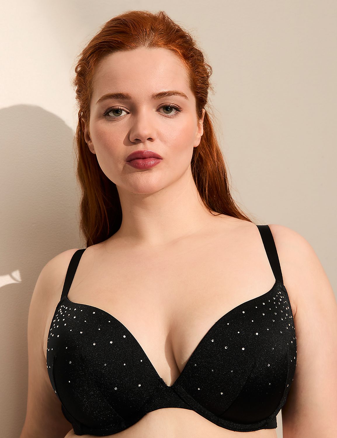 A woman with red hair poses in a black, studded bra against a plain, shadowed background. Product Image 1