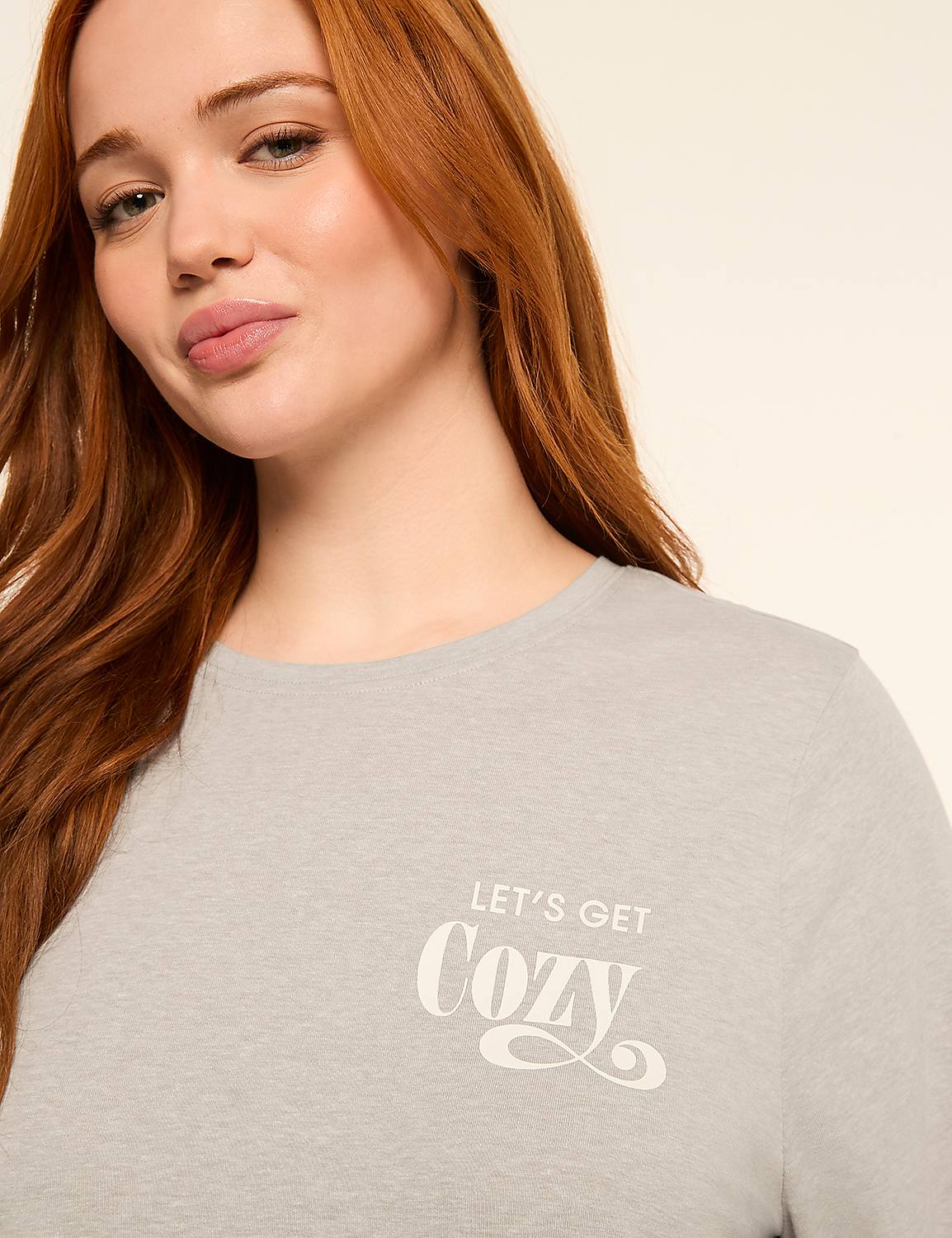 A woman with red hair smiles softly in the foreground, wearing a light gray t-shirt with the words "LET'S GET COZY" printed on it, against a plain, light-colored background. Product Image 4