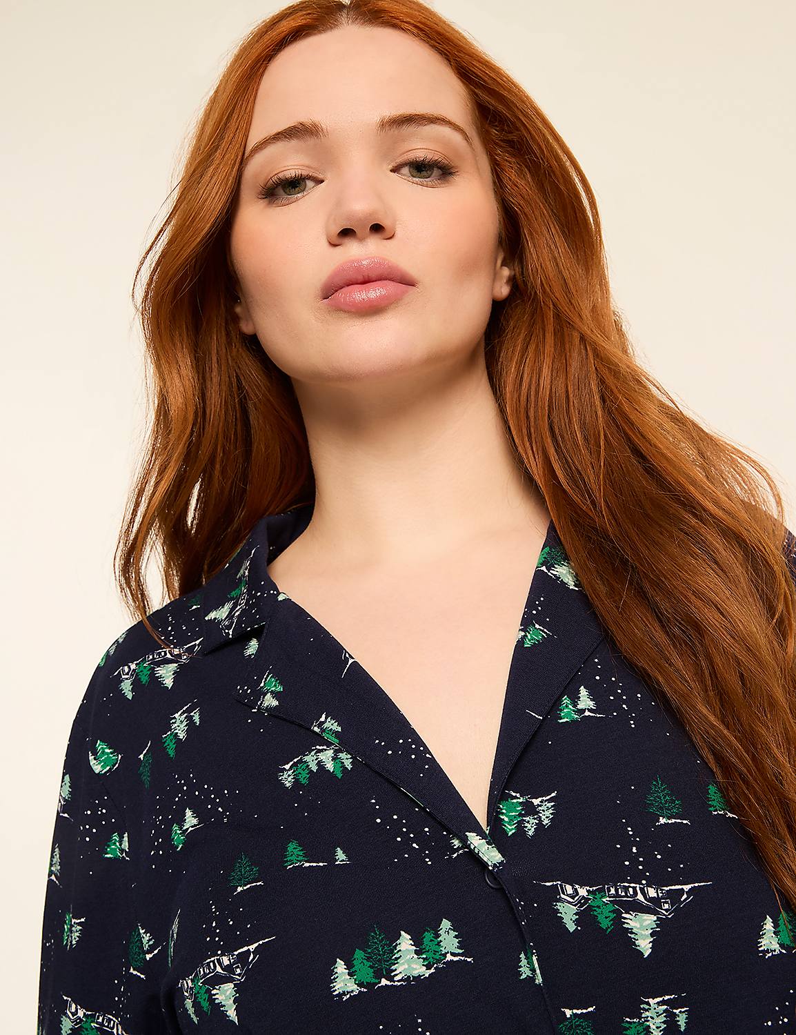 A woman with long, red hair looks forward, wearing a dark blue shirt with a pattern of green trees and white snow. Product Image 4