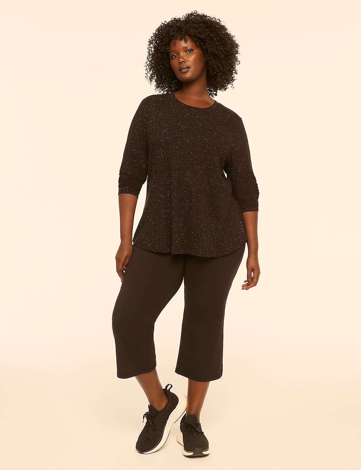 A smiling plus-size woman in a grey sports bra and black capri leggings stands against a plain, light-colored background. Product Image 3