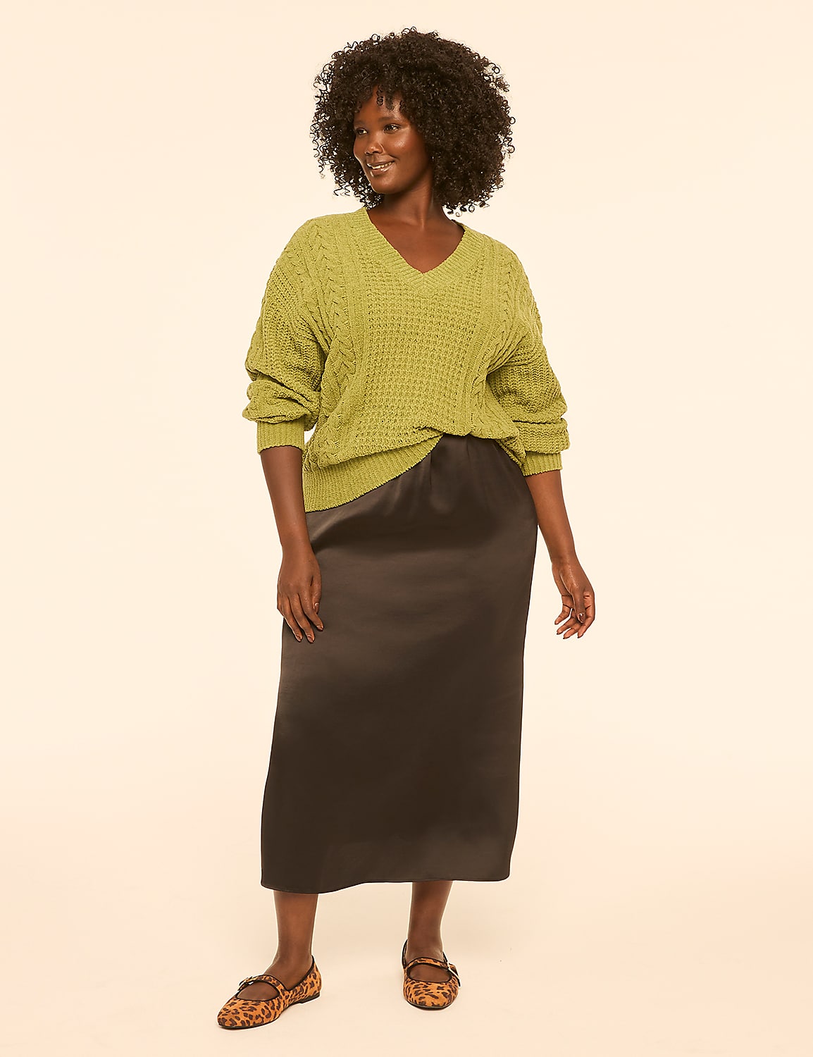 A woman in a green cable-knit sweater and a black satin skirt stands against a plain, light-colored background. Product Image 3