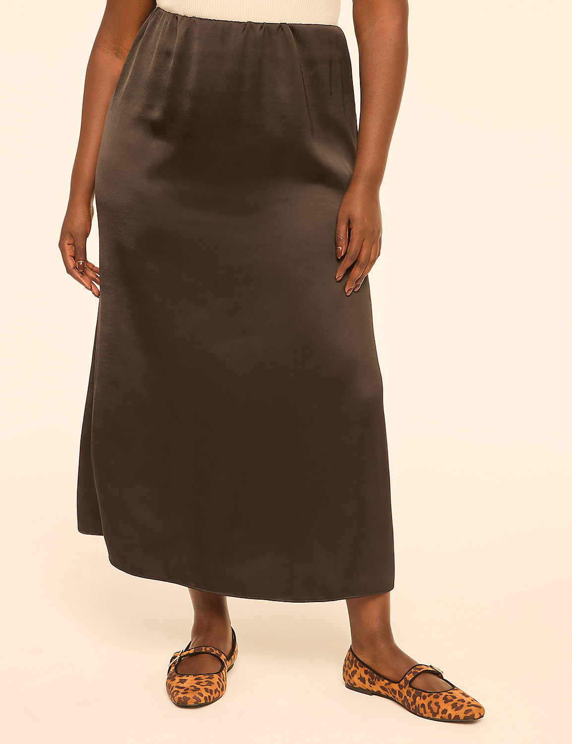 A person stands in a studio setting wearing a dark satin skirt and leopard print flats against a plain, light-colored background. Product Image 1