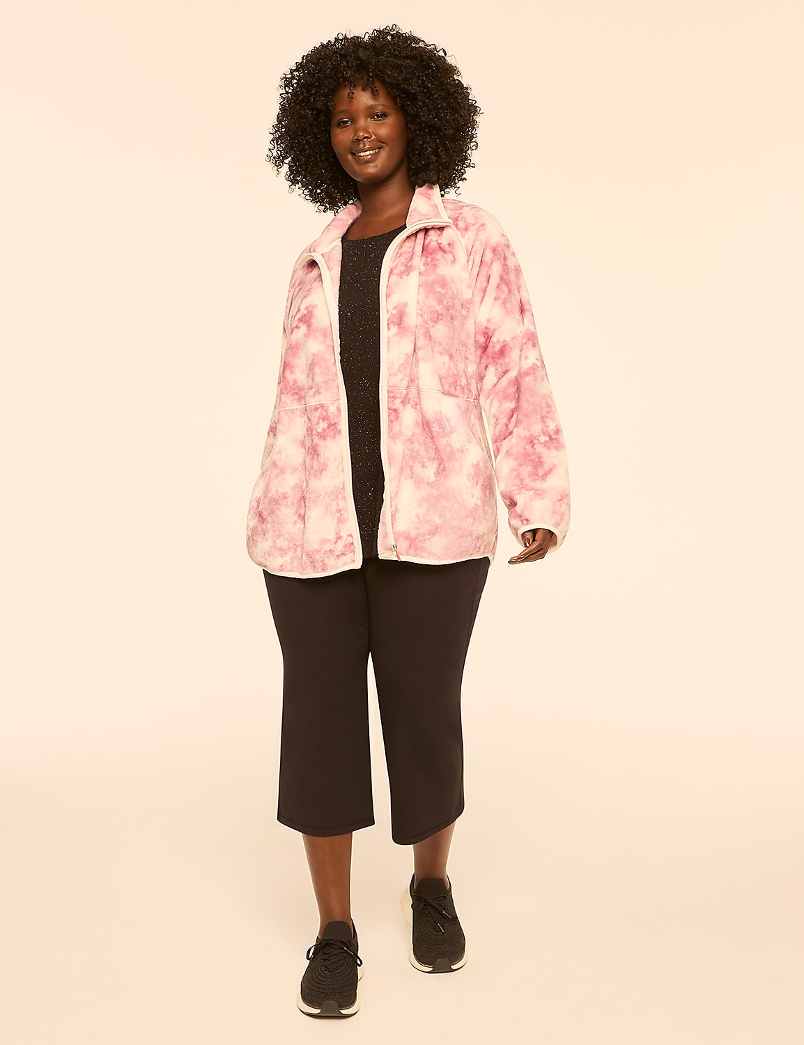 A woman with dark curly hair smiles as she stands in a pink and white tie-dye jacket over a dark dress and black shoes, against a plain cream background. Product Image 3