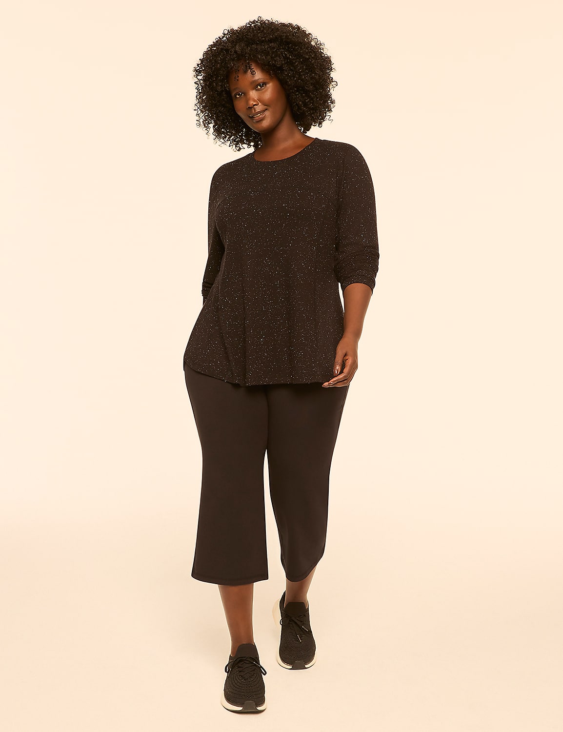 A woman with dark, curly hair stands in the foreground wearing a sparkly black top and black capri pants against a plain, light-colored background. Product Image 3