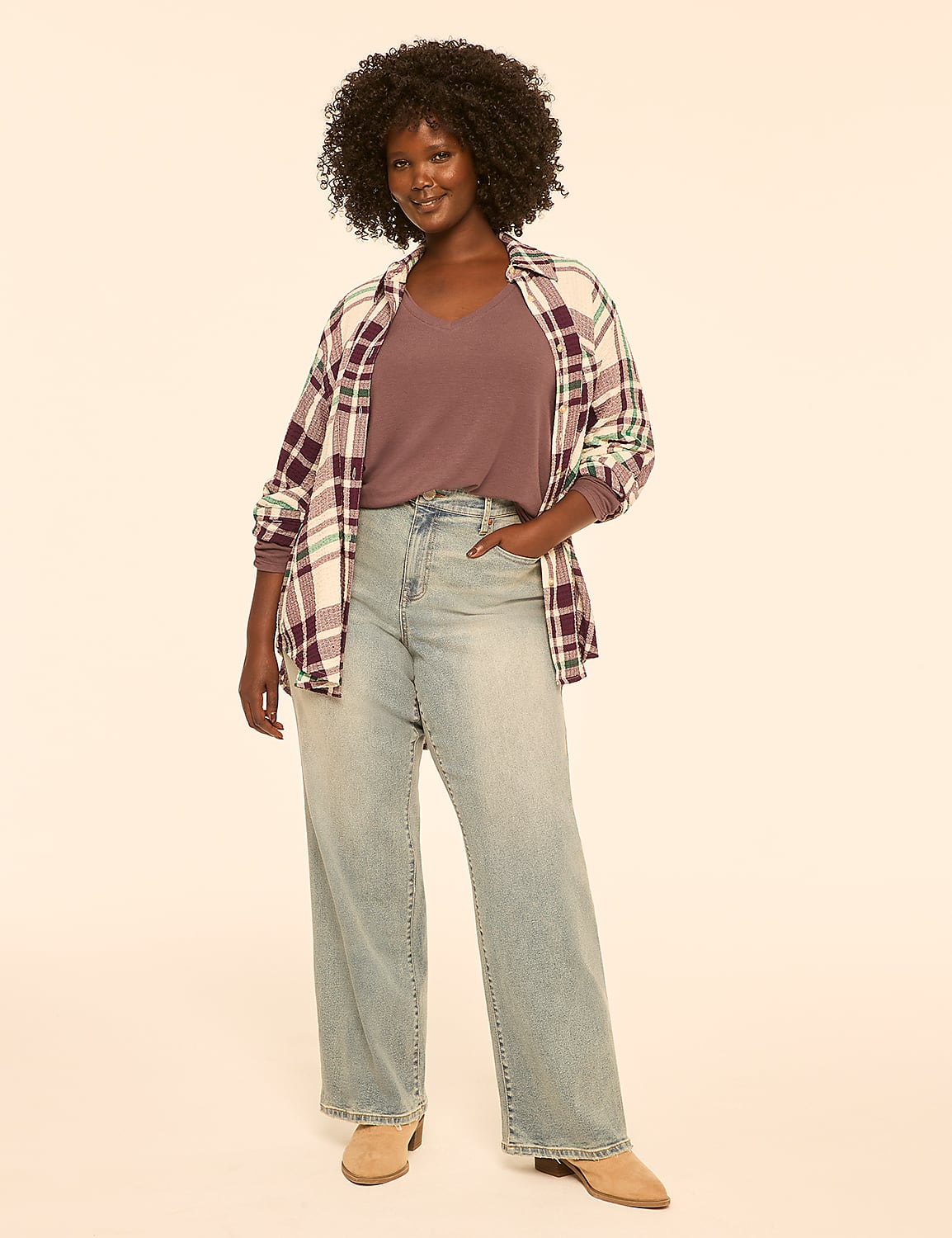 A woman with dark curly hair stands in the foreground wearing a purple v-neck shirt, an open plaid shirt, and light-wash wide-leg jeans, against a plain, light-colored background. Product Image 3