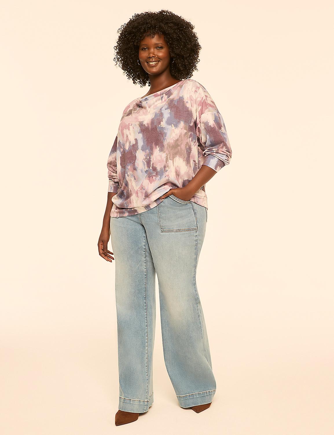 A woman with dark, curly hair stands in the foreground wearing a tie-dye sweatshirt and wide-leg jeans against a plain, light-colored background. Product Image 3