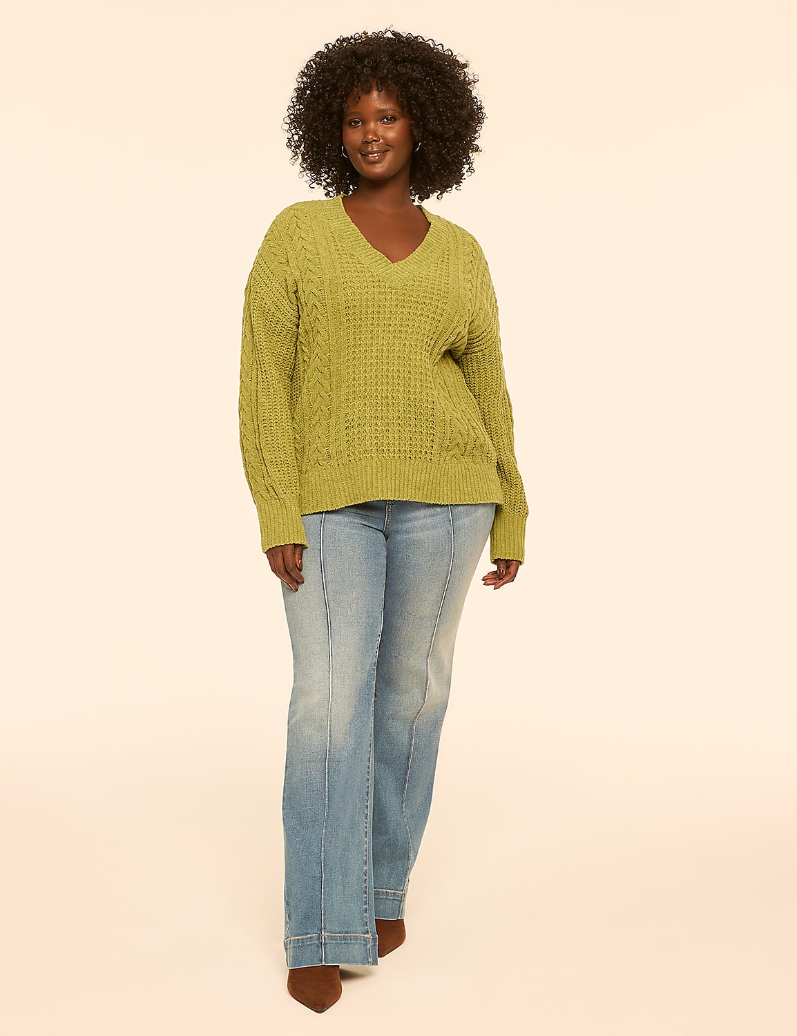 A woman in a green cable-knit sweater and light-wash jeans stands against a plain, light-colored background. Product Image 3