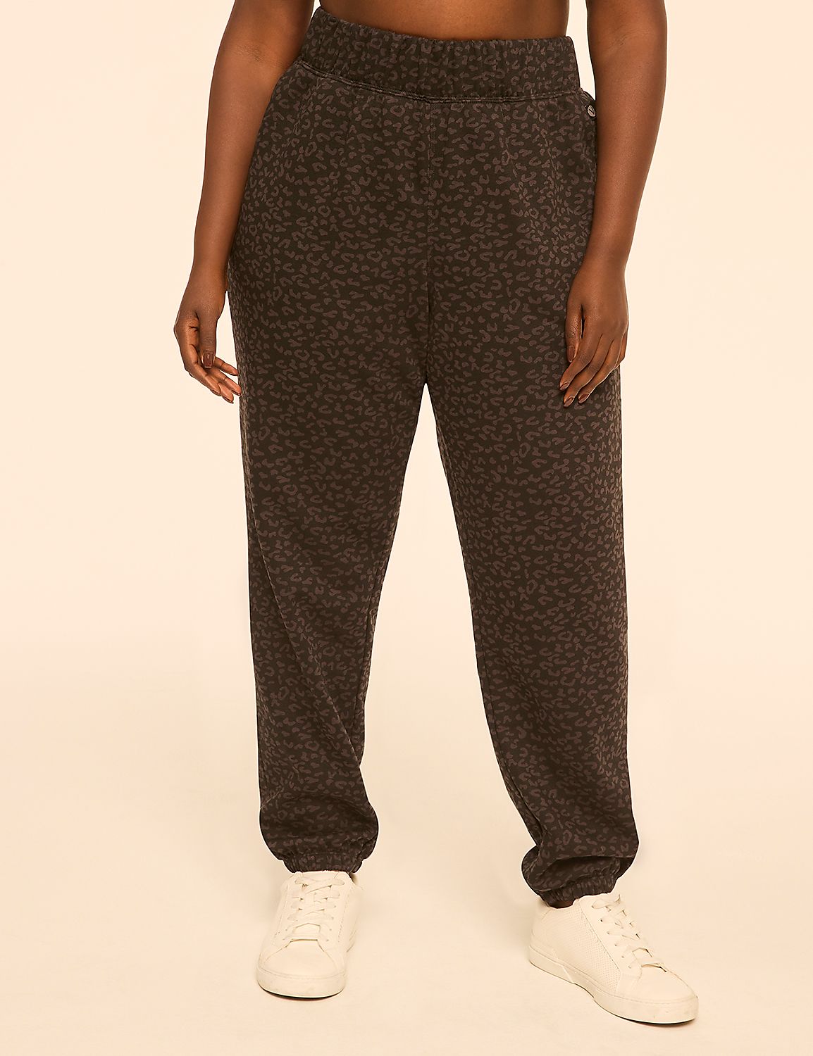 A person wearing leopard-print sweatpants and white sneakers stands against a plain, peachy-toned background. Product Image 1