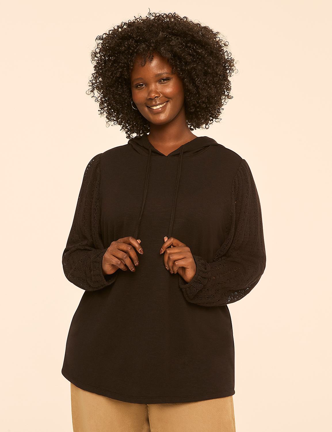 A smiling woman with dark, curly hair stands in the foreground wearing a black hooded sweatshirt, against a plain, light-colored background. Product Image 1