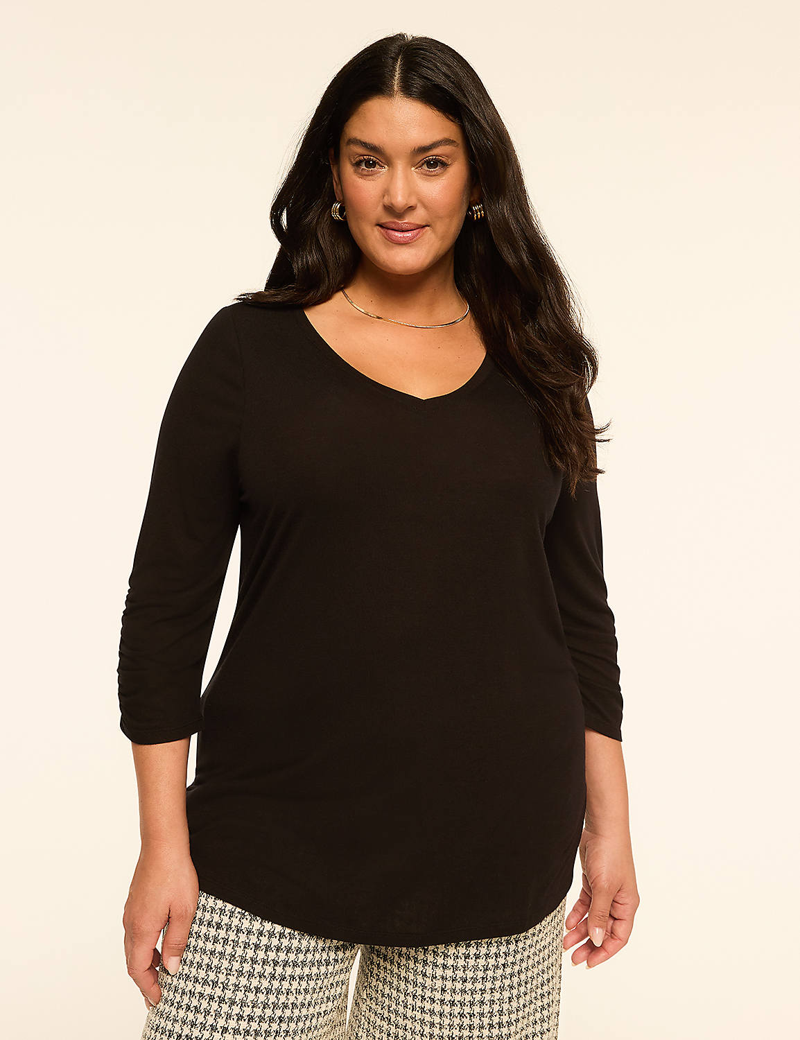 A woman in a black v-neck shirt and patterned pants stands against a plain, light-colored background. Product Image 1