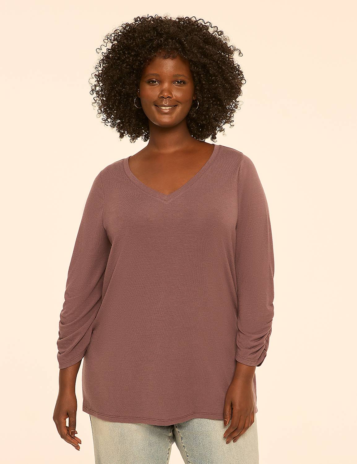 A smiling woman with curly dark hair and a mauve v-neck shirt stands against a plain, light-colored background. Product Image 1