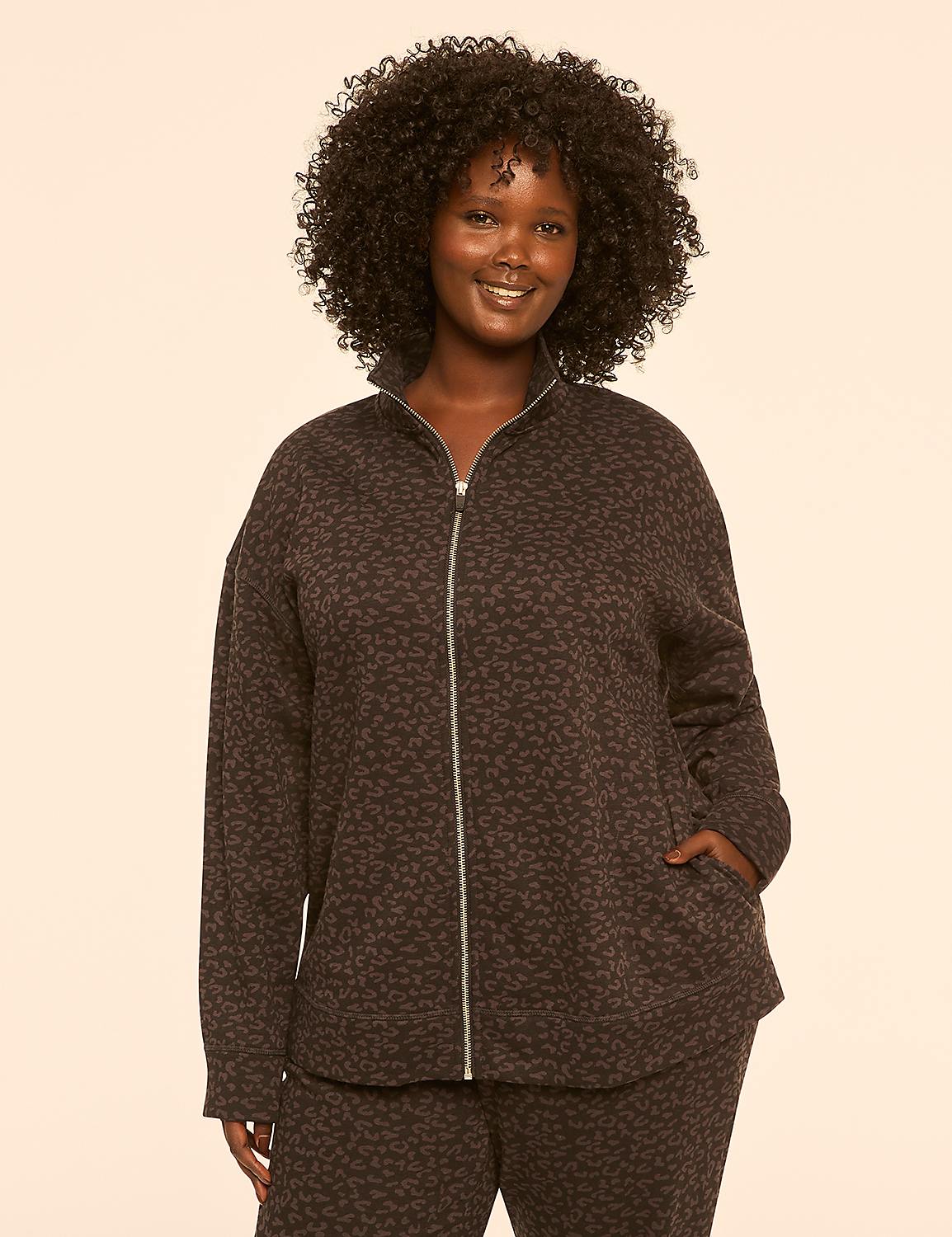 A smiling woman with curly dark hair stands in the foreground wearing a leopard-print zip-up jacket and matching pants against a plain, light-colored background. Product Image 1