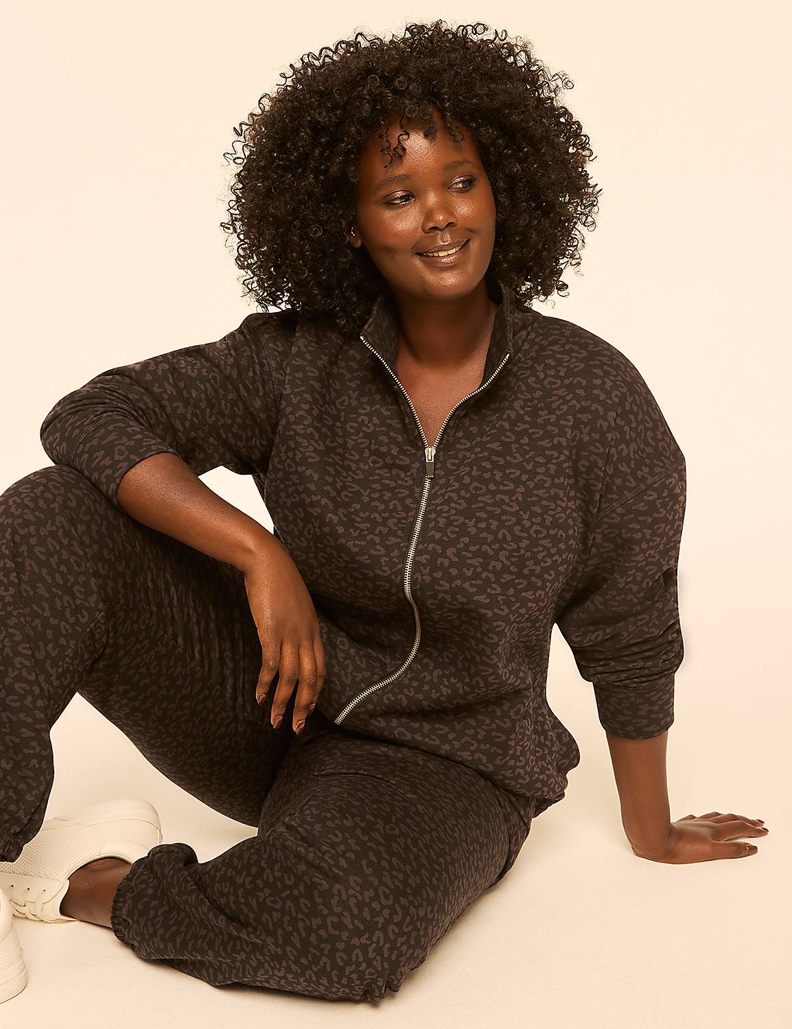 A woman with dark, curly hair and a leopard-print tracksuit sits on a plain, light-colored background. Product Image 3