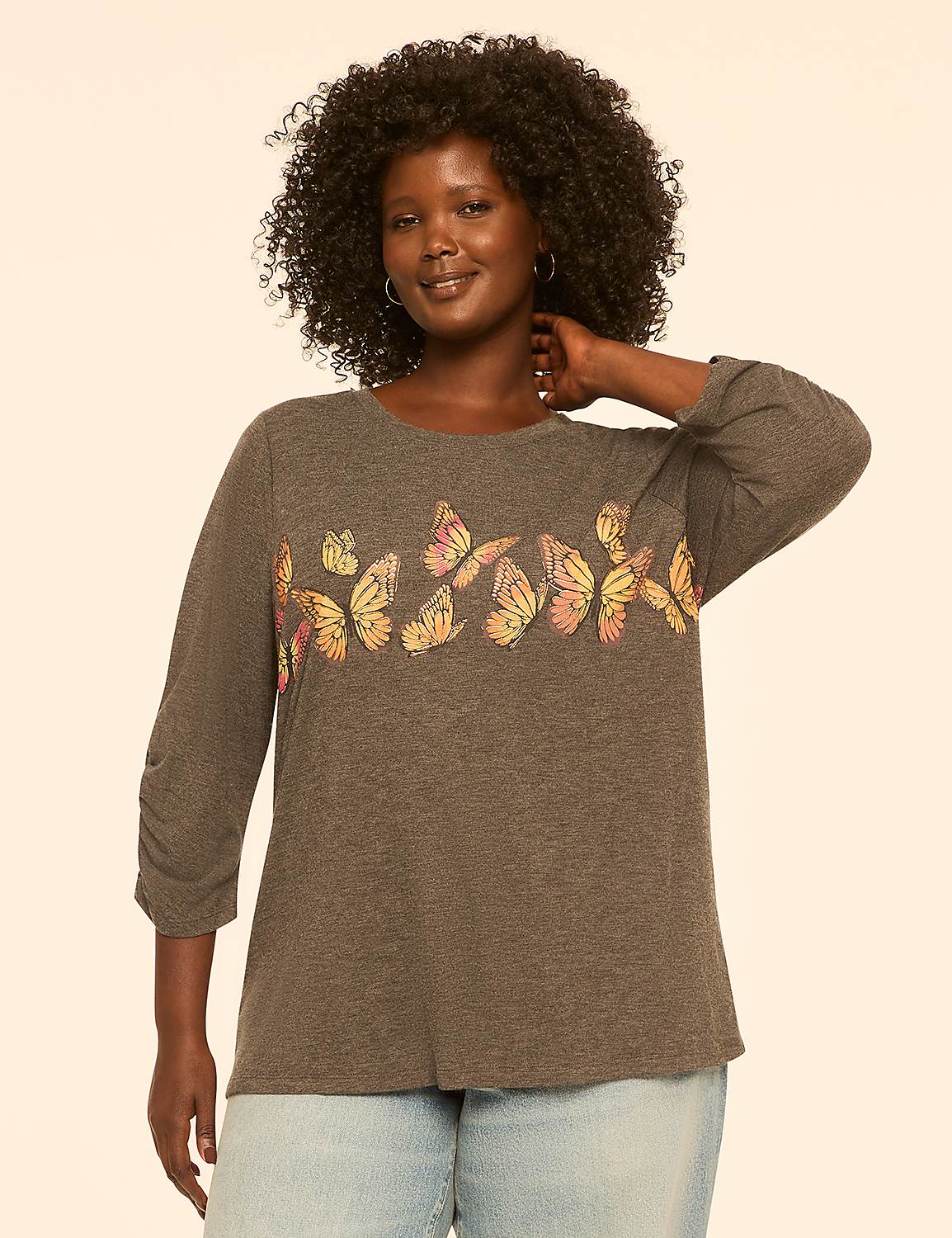A woman with curly dark hair and a warm smile poses in a grey t-shirt adorned with colorful butterflies, set against a plain, light-colored background. Product Image 1