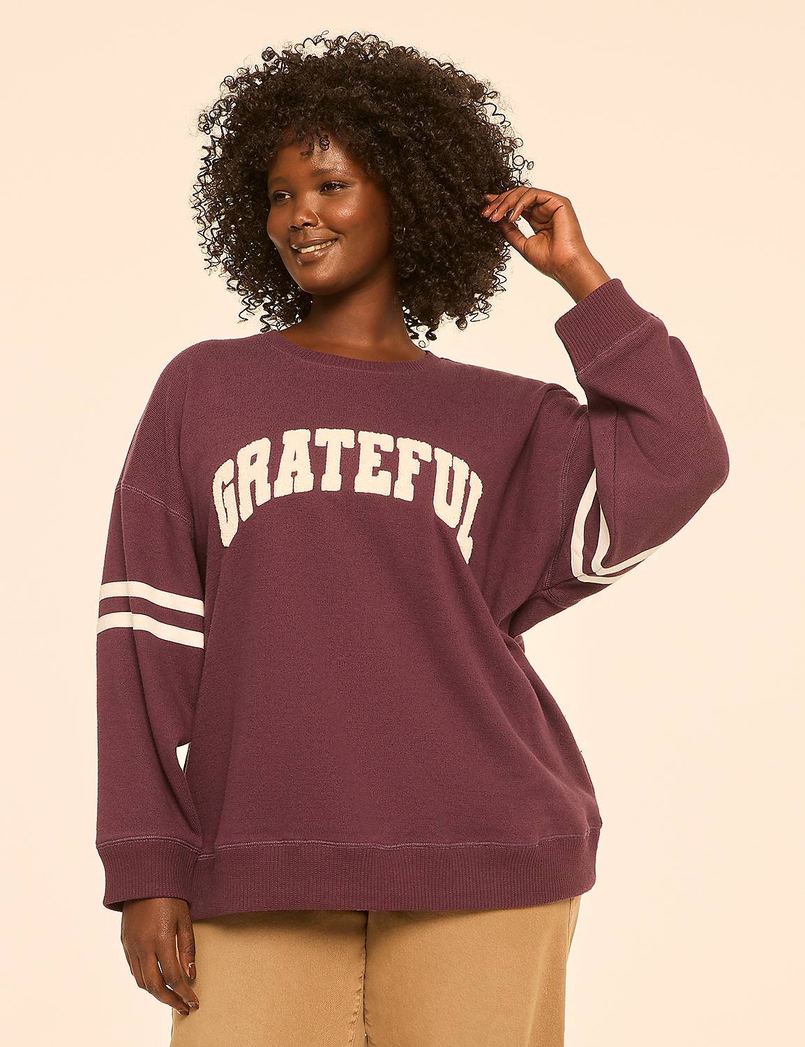 A woman with curly dark hair smiles as she poses in a maroon sweatshirt with "GRATEFUL" written across the chest, against a plain, light-colored background. Product Image 1