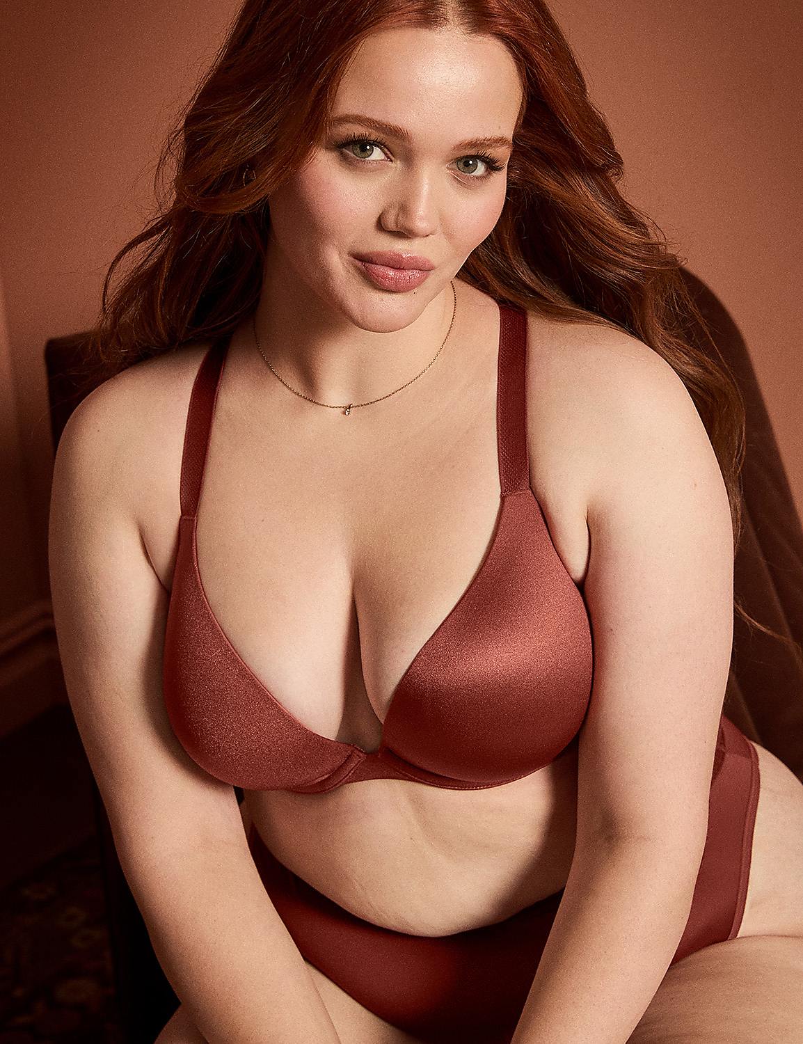 A woman with red hair and a red bra sits in front of a blurred background. Product Image 6