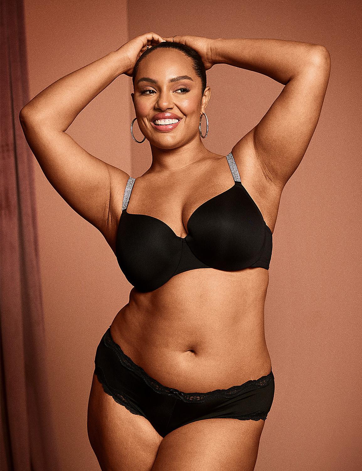 A smiling woman in black lingerie poses with her hands behind her head against a warm, textured background. Product Image 5