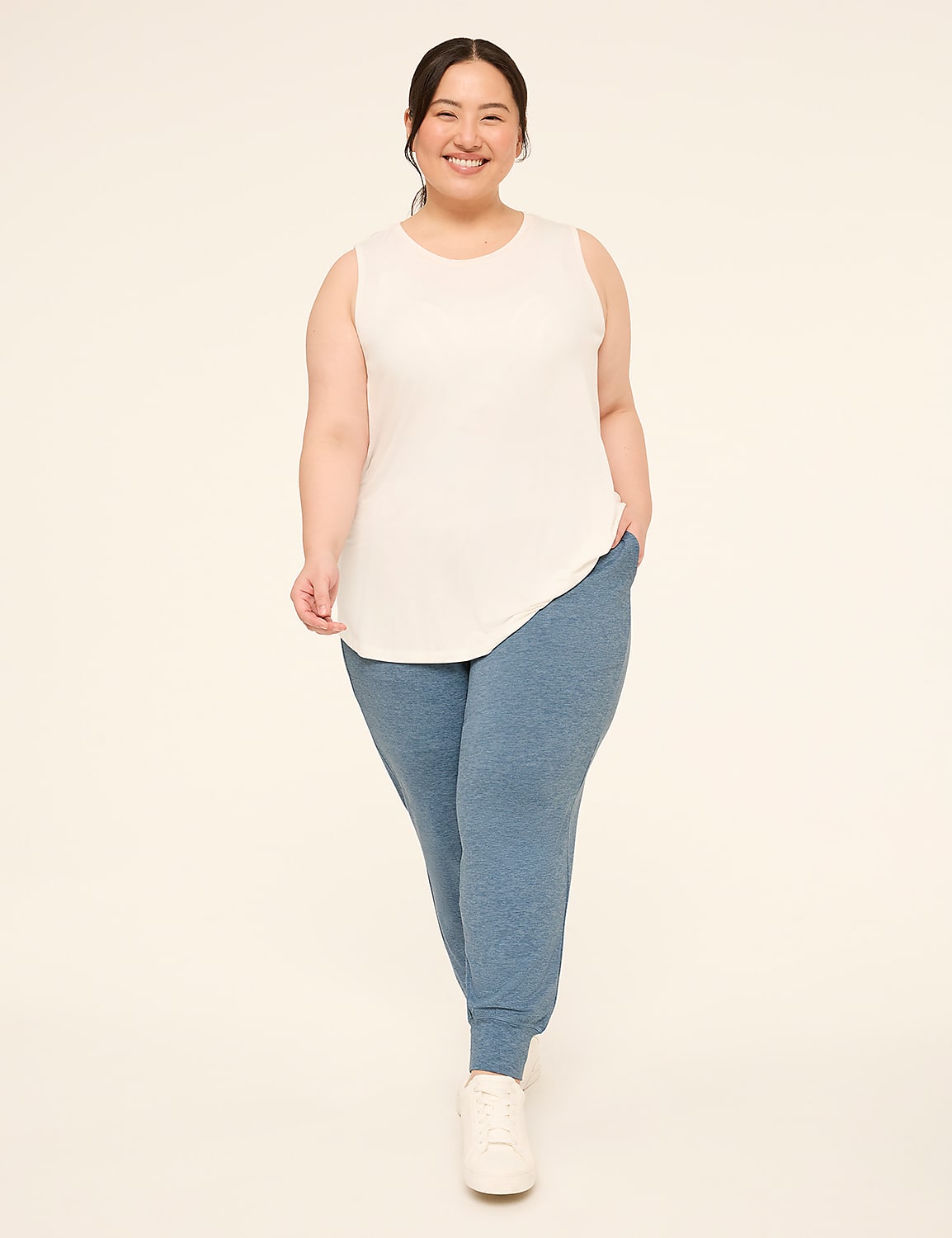 A smiling woman in a white tank top and blue joggers stands against a plain, light-colored background. Product Image 3