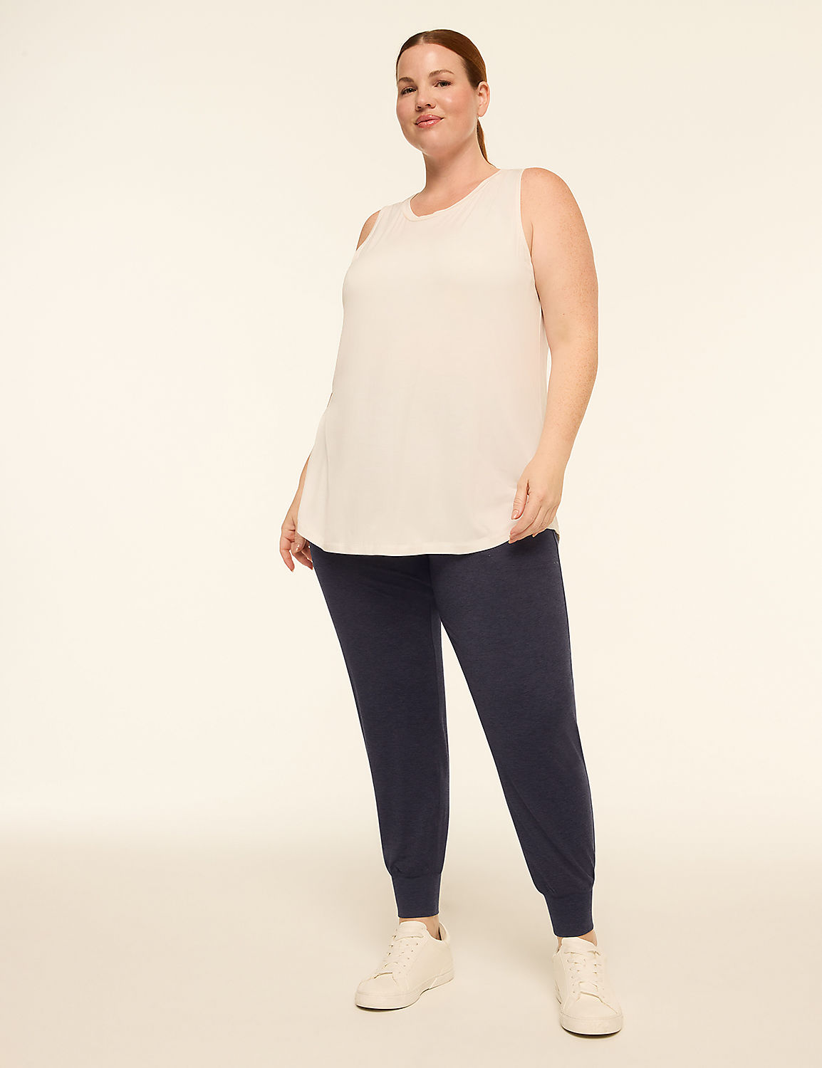 A woman in a light pink tank top and dark blue joggers stands against a plain, light background. Product Image 3