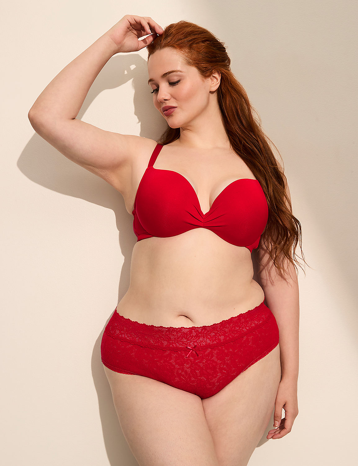 A woman with red hair in a red bra and panties poses against a plain, light-colored wall with soft shadows. Product Image 3