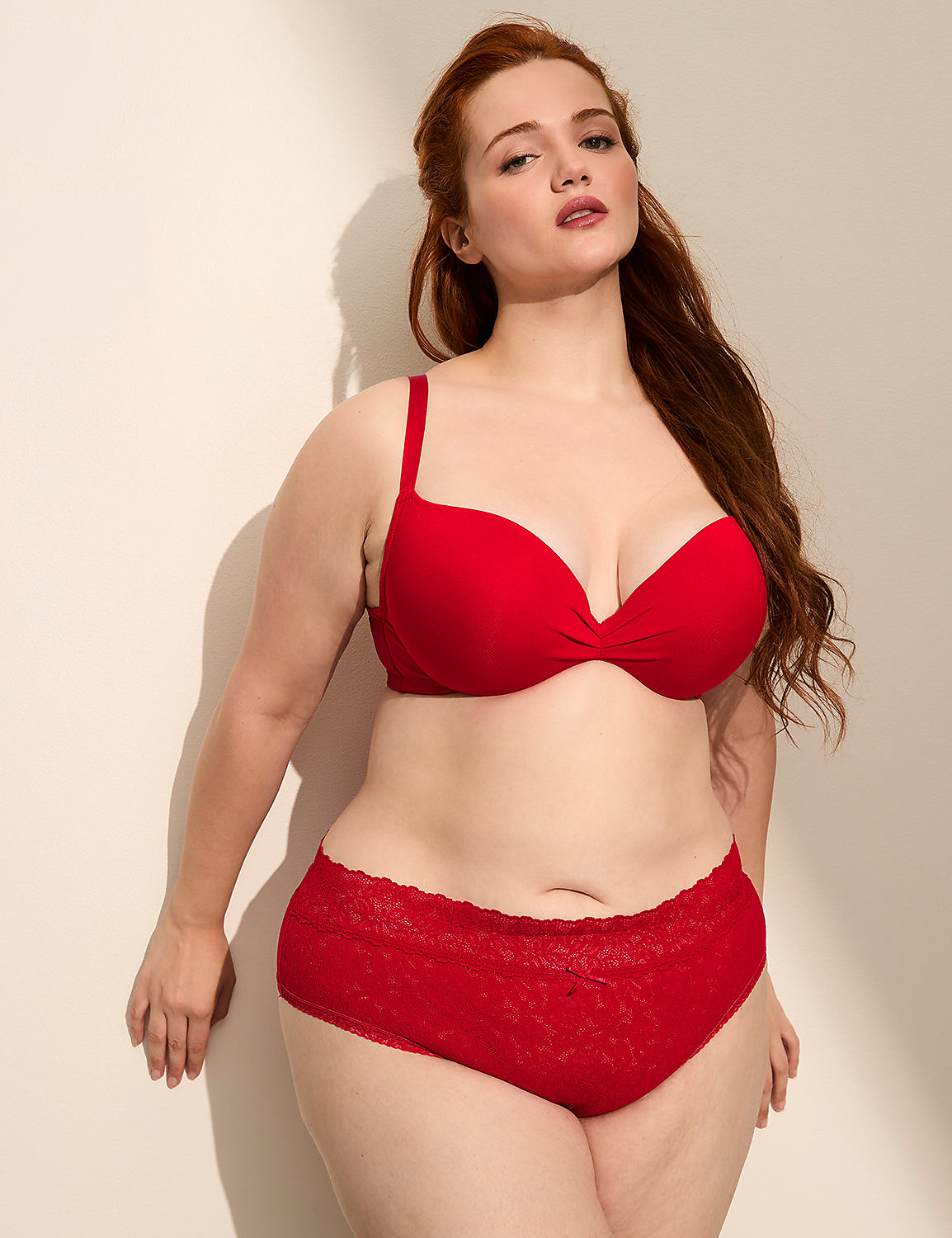 A woman with red hair in a red bra and panties stands against a plain, light-colored wall with shadows. Product Image 3
