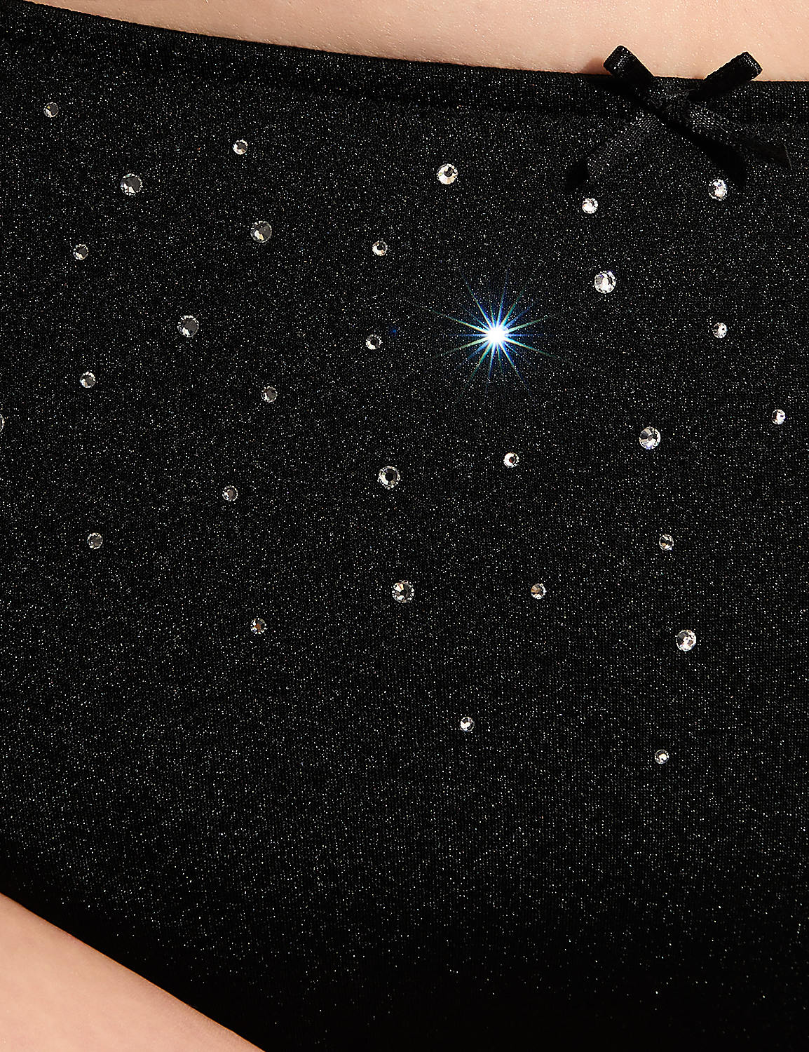 A black, sparkly garment adorned with rhinestones and a small bow is shown against a blurred, light-colored background. Product Image 4