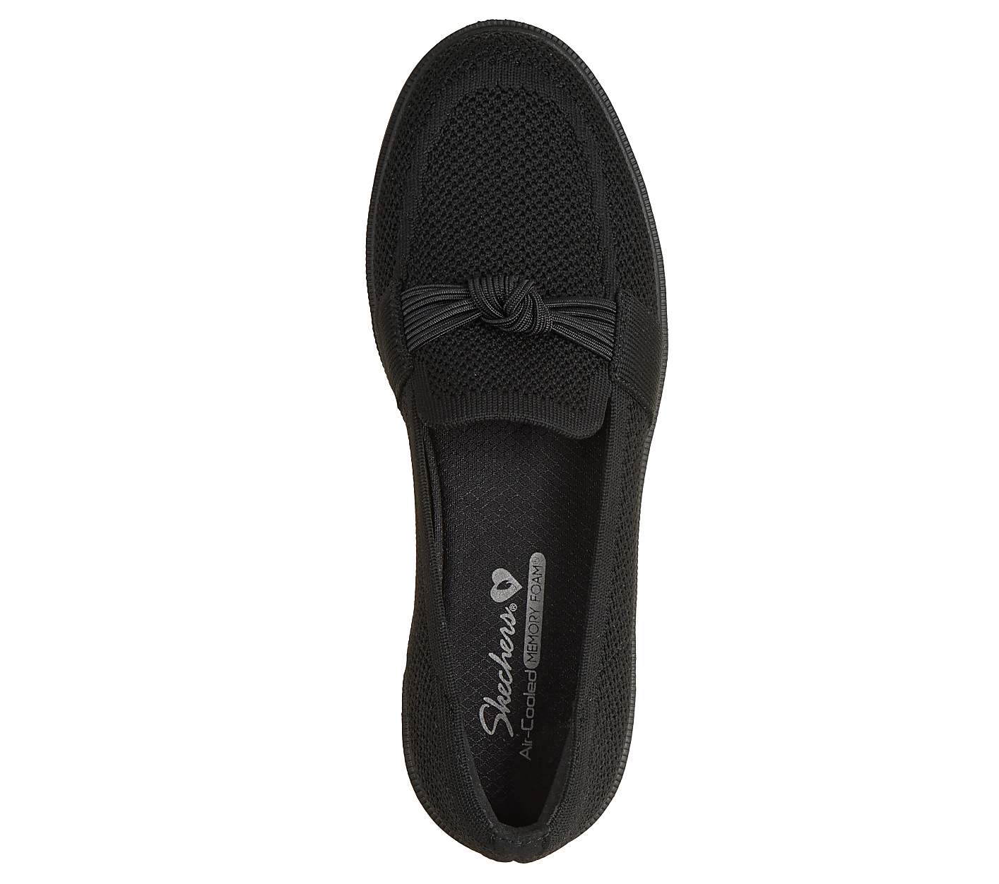 A black Skechers loafer with a knotted bow detail in the foreground rests on a plain white background. Product Image 2