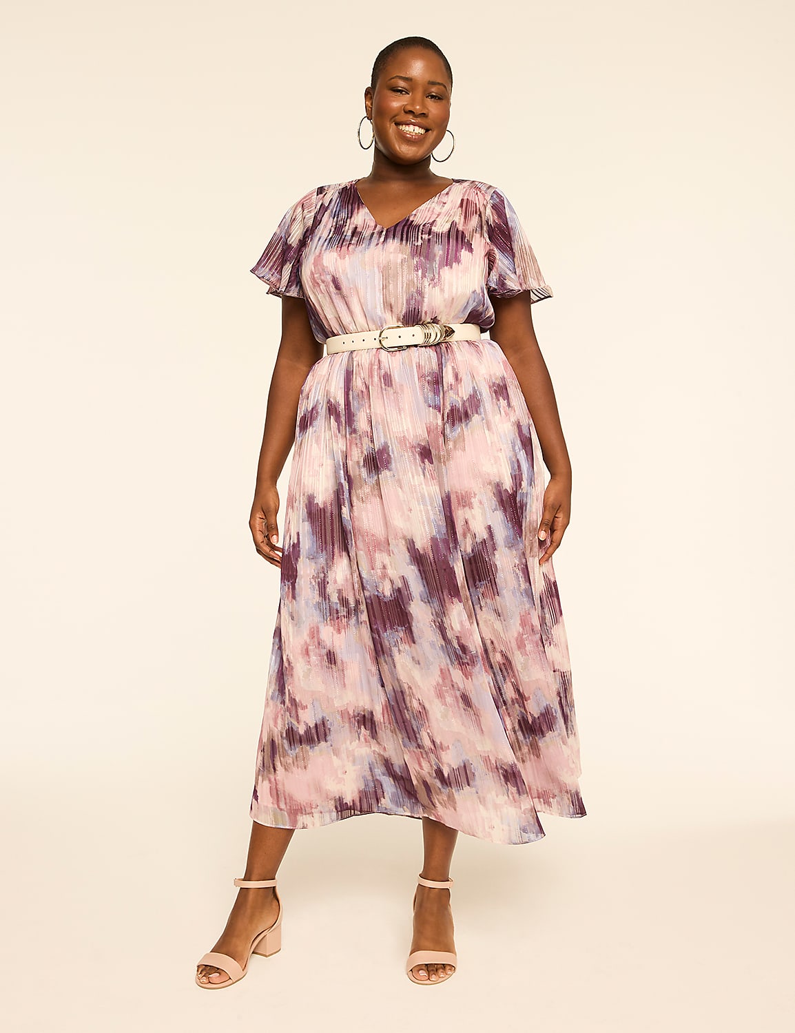 A smiling woman in a flowing, abstract-print dress and light-colored belt stands against a plain, light-colored background. Product Image 1