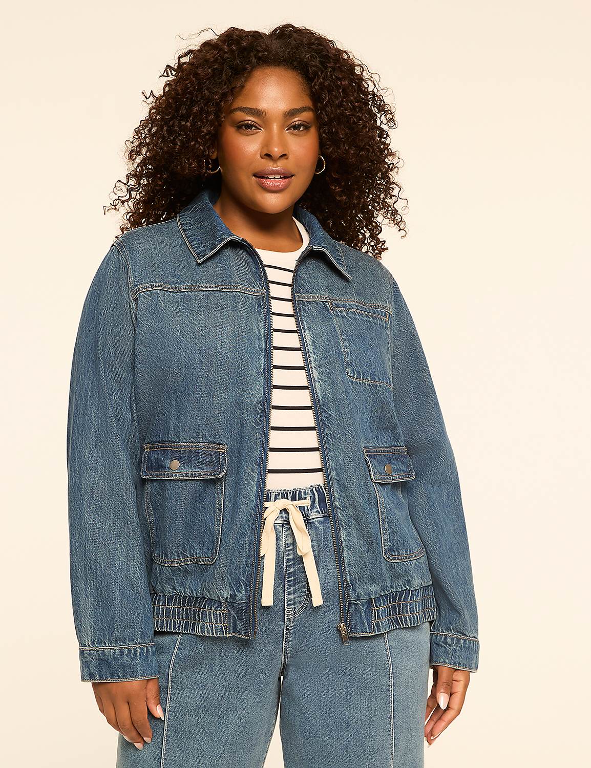 A woman in a denim jacket and striped shirt stands against a plain, light-colored background. Product Image 1