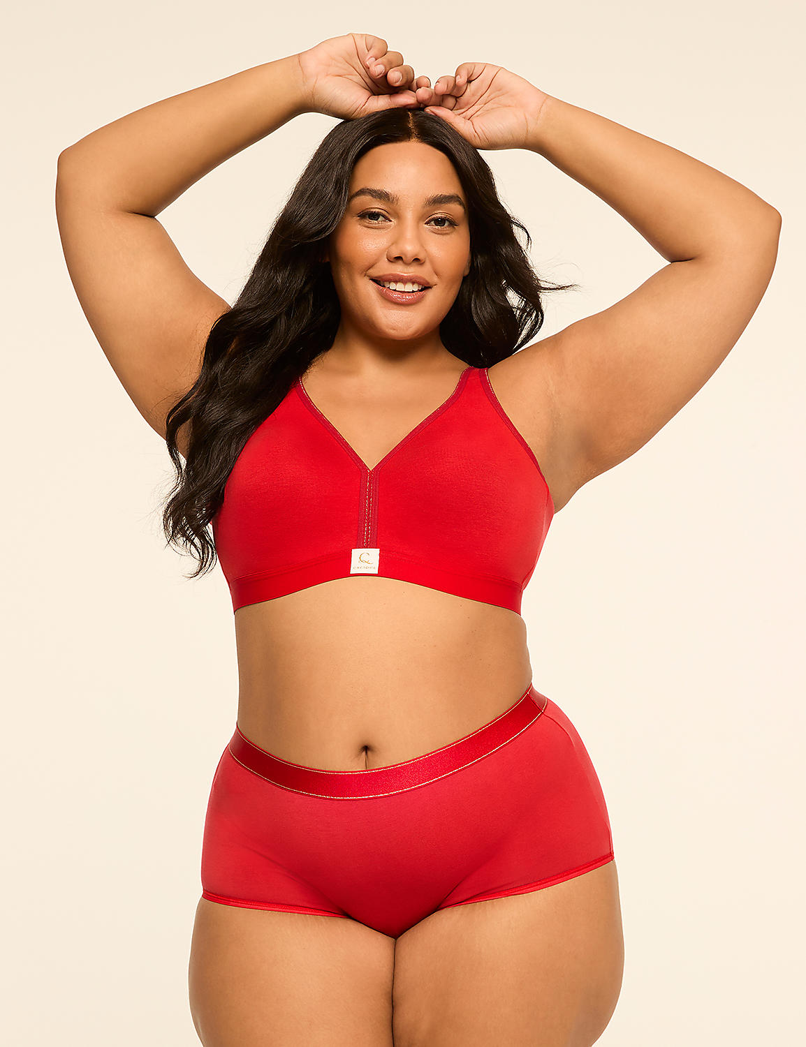 A smiling woman in a red bra and matching underwear poses with her hands above her head against a plain cream background. Product Image 4