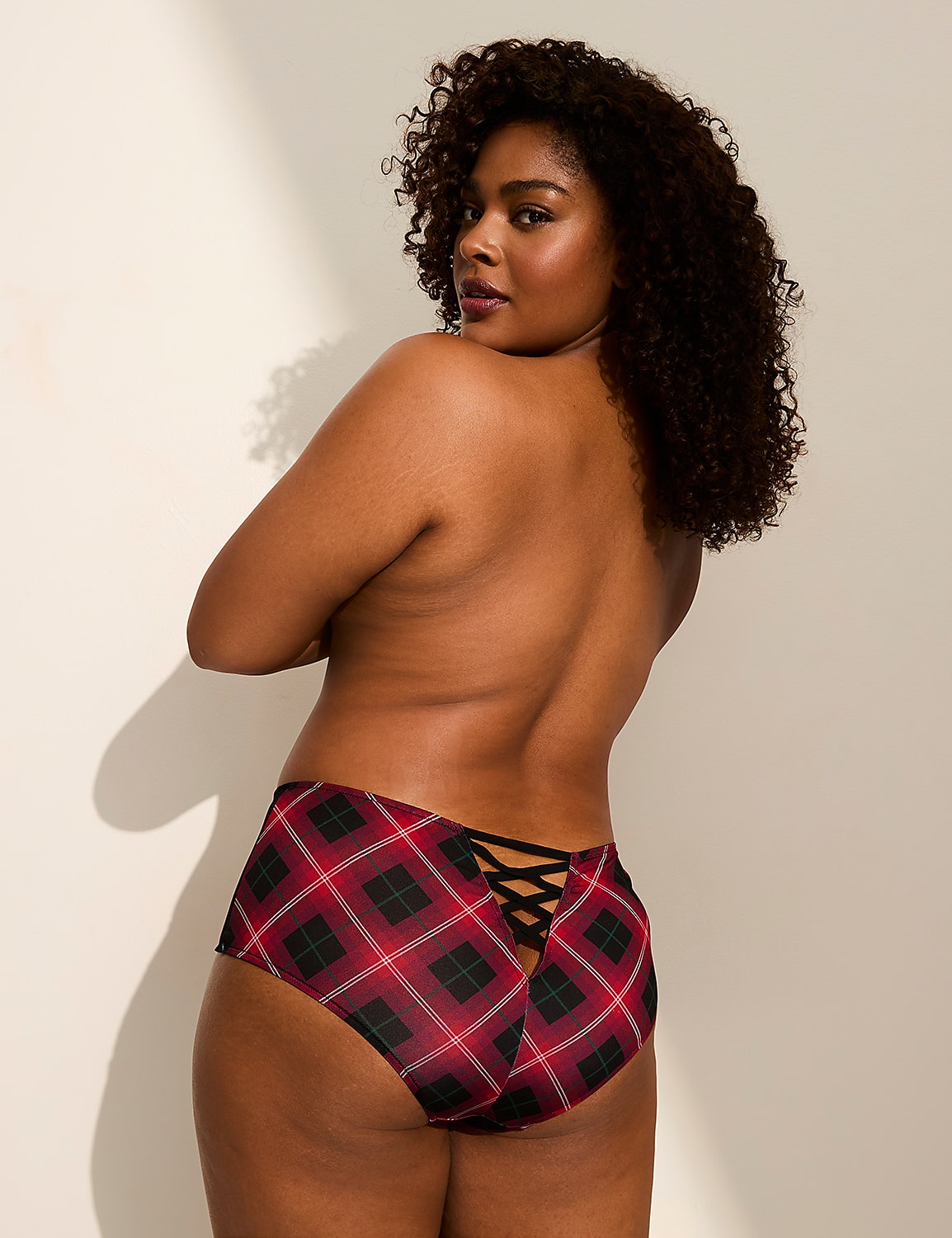 A woman with curly hair poses with her back to the camera, wearing plaid underwear with a lace-up detail, against a plain, light-colored wall. Product Image 3