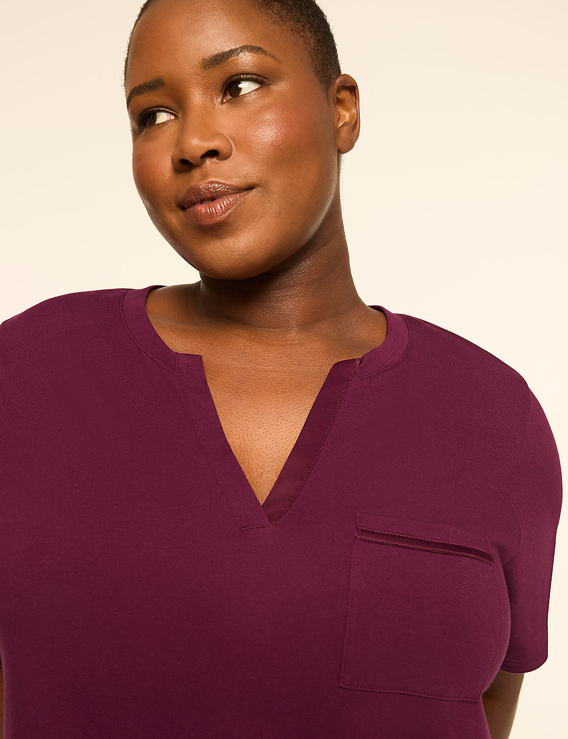 A woman with dark skin and short hair, wearing a plum-colored V-neck shirt with a chest pocket, is shown against a plain, light-colored background. Product Image 3