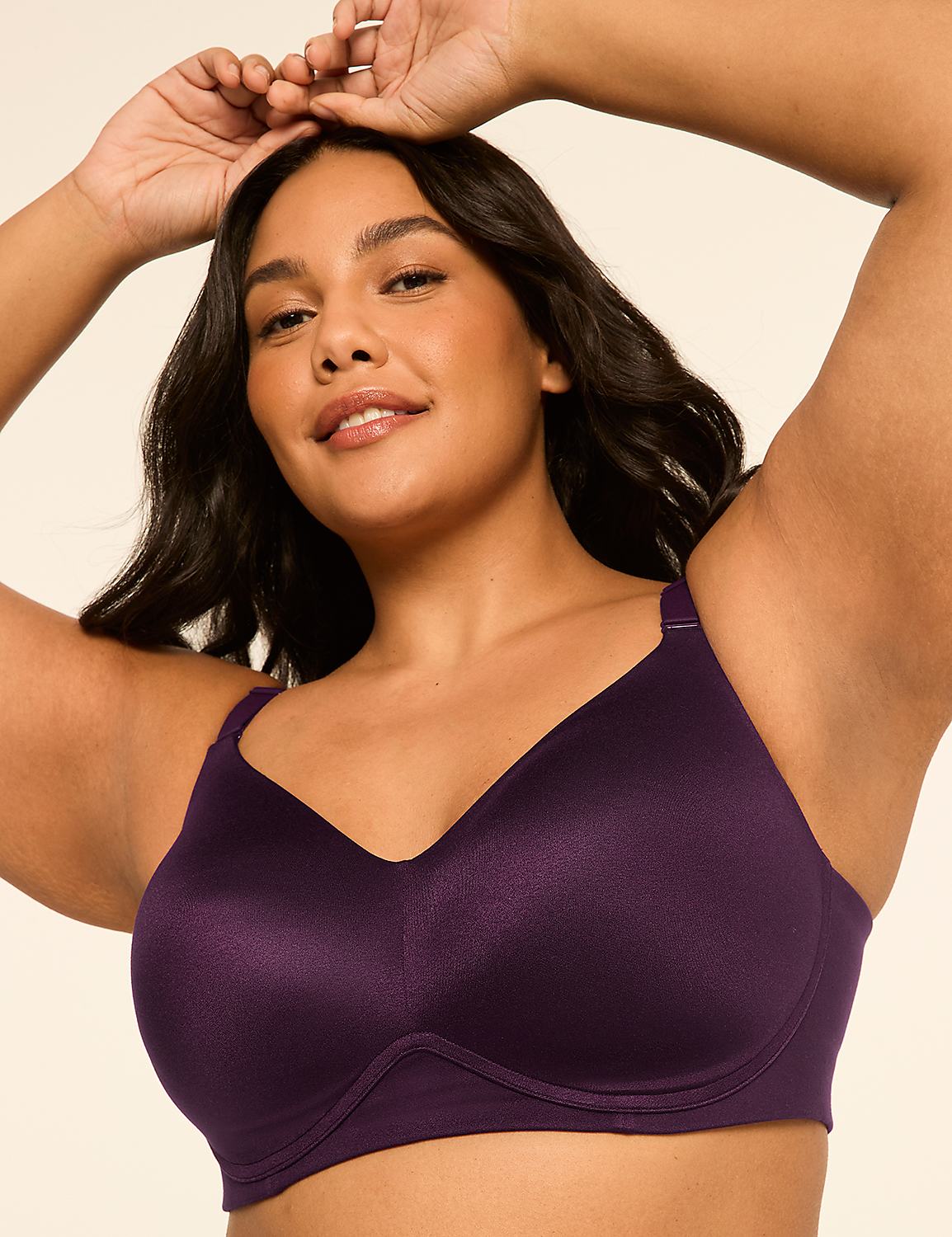 A woman with dark hair and a warm smile poses with her arms raised, wearing a deep purple bra against a plain, light background. Product Image 1