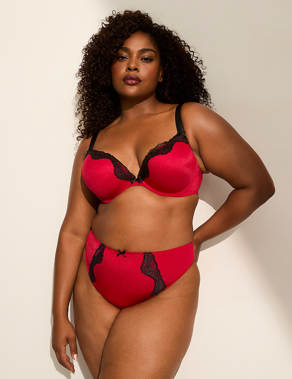 A woman in a red and black lace bra and matching underwear stands against a plain, light-colored background with a shadow on the right. Product Image 4