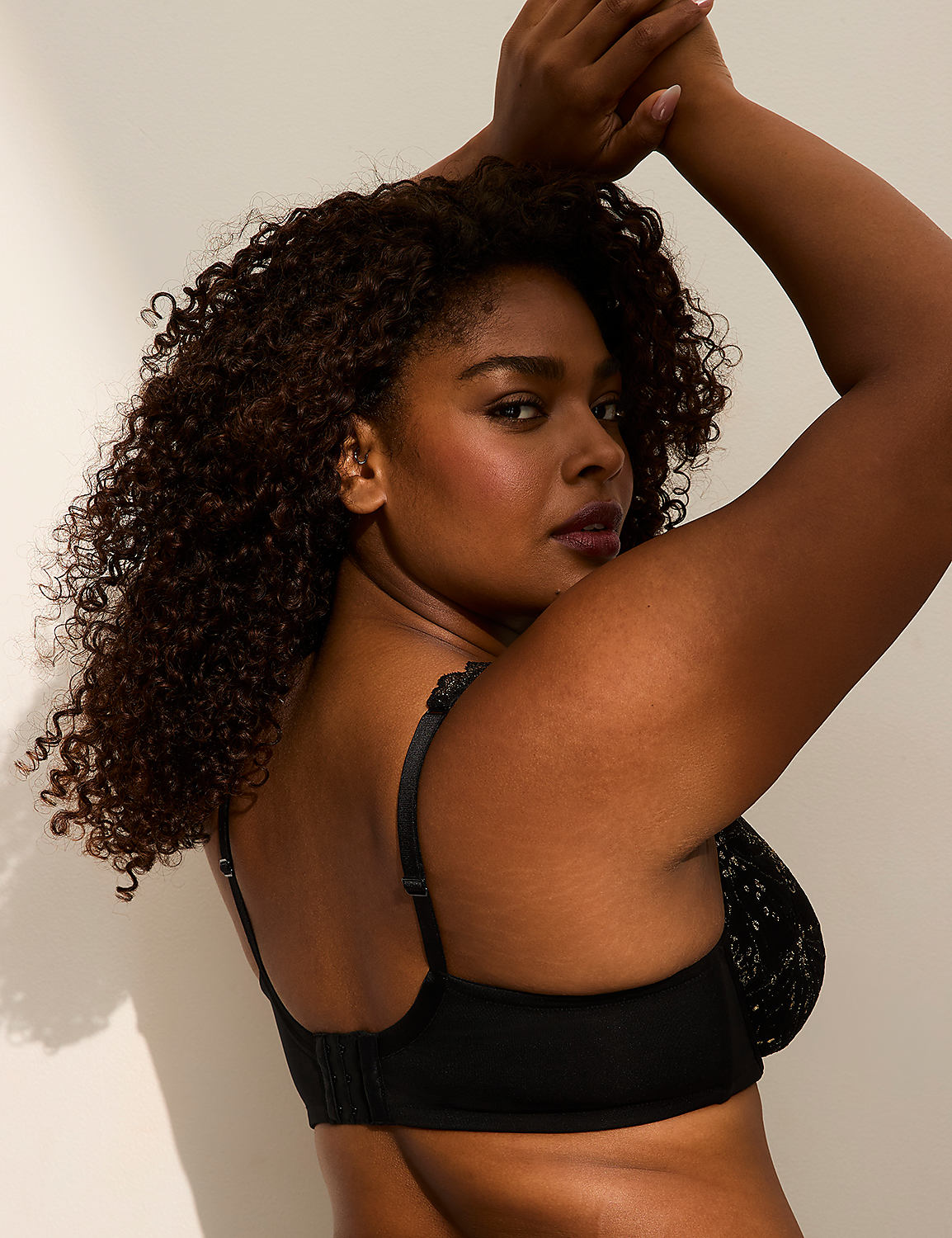 A woman with curly dark hair poses in a black lace bra against a plain white background. Product Image 5
