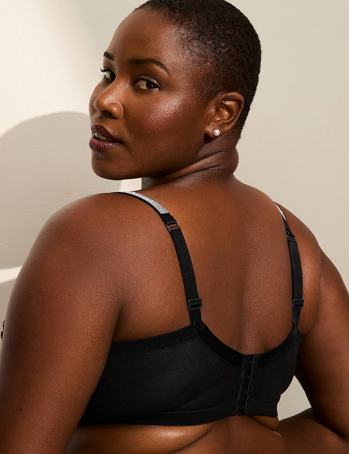A woman with short hair looks over her shoulder, wearing a black bra against a softly lit, neutral background. Product Image 3