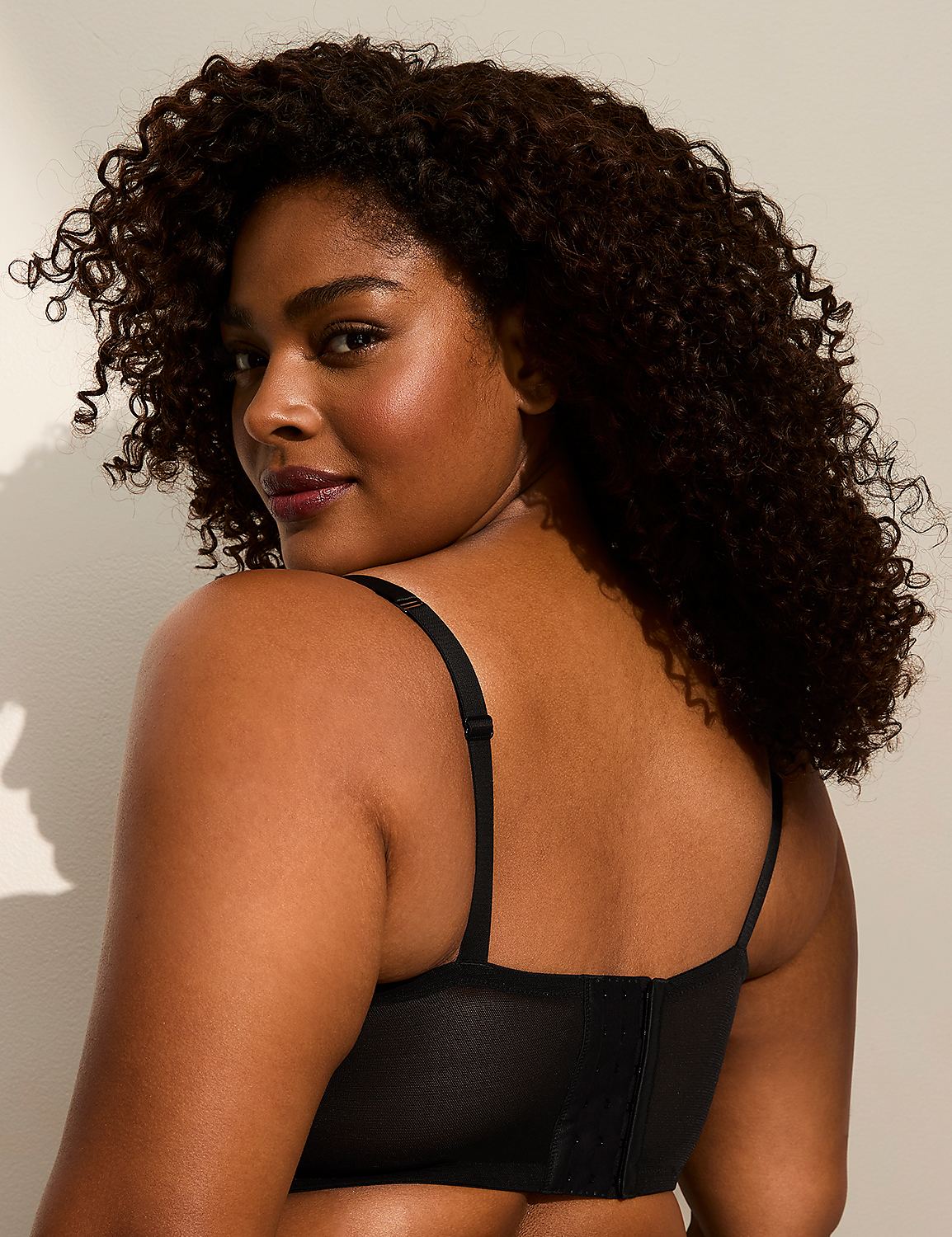 A woman with curly dark hair and a black bra is shown from the back, with a plain, light-colored background. Product Image 3