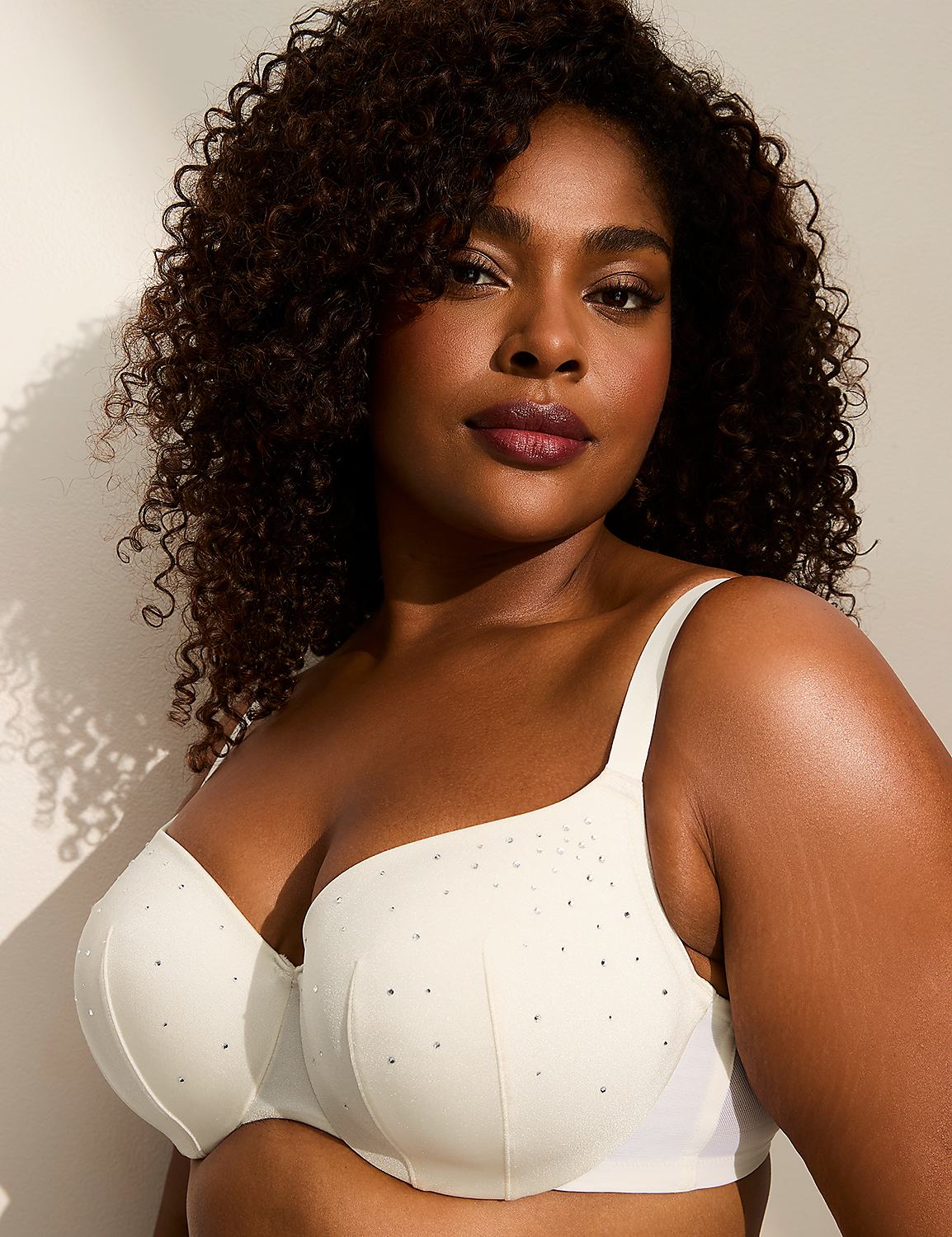 A woman with dark curly hair and makeup poses in a white bra adorned with rhinestones against a plain, light-colored background. Product Image 1