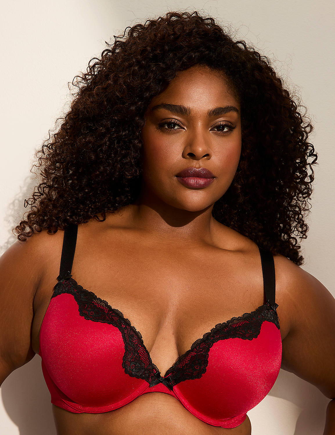 A woman with dark, curly hair wears a red bra with black lace trim, set against a plain, light-colored background. Product Image 1