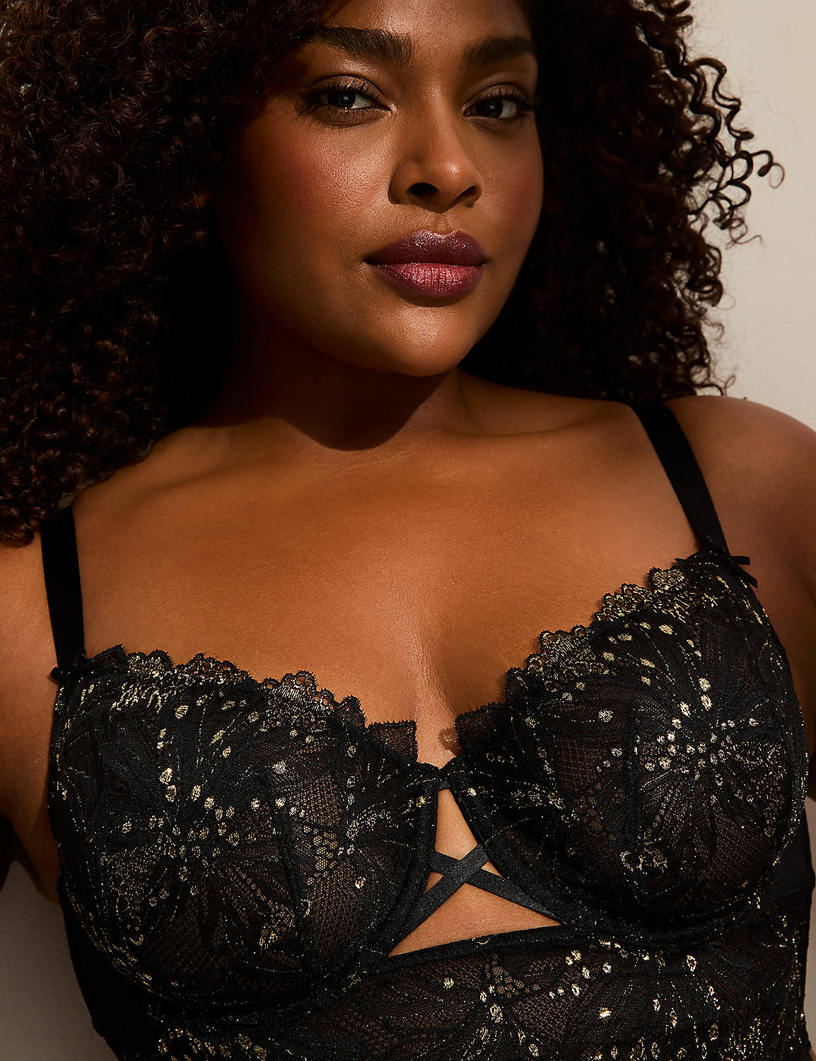 A woman with curly dark hair and dark eyes wears a black lace bra with gold accents, against a plain background. Product Image 2