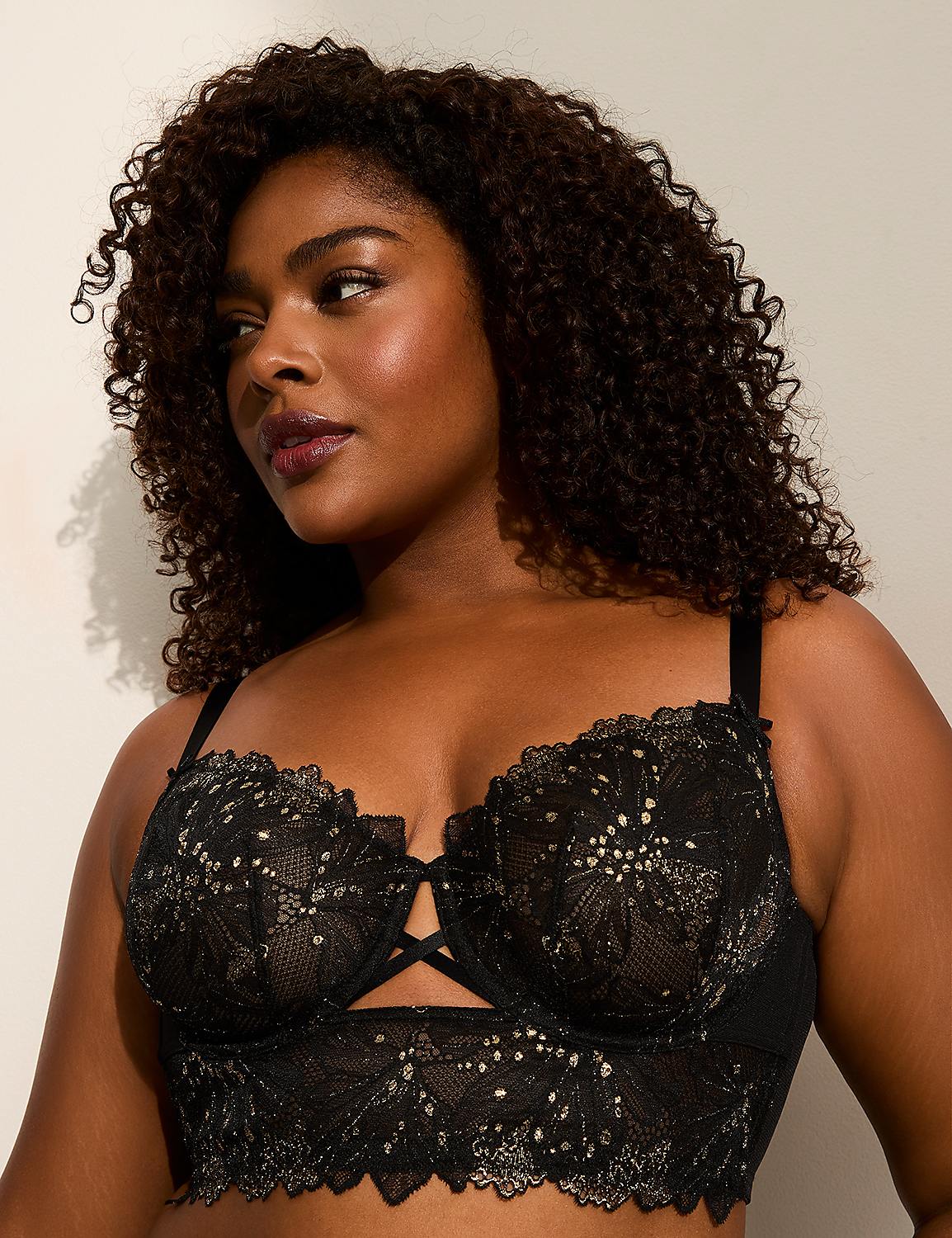 A woman with curly dark hair wears a black lace longline bra with gold accents, set against a plain, light-colored background. Product Image 1