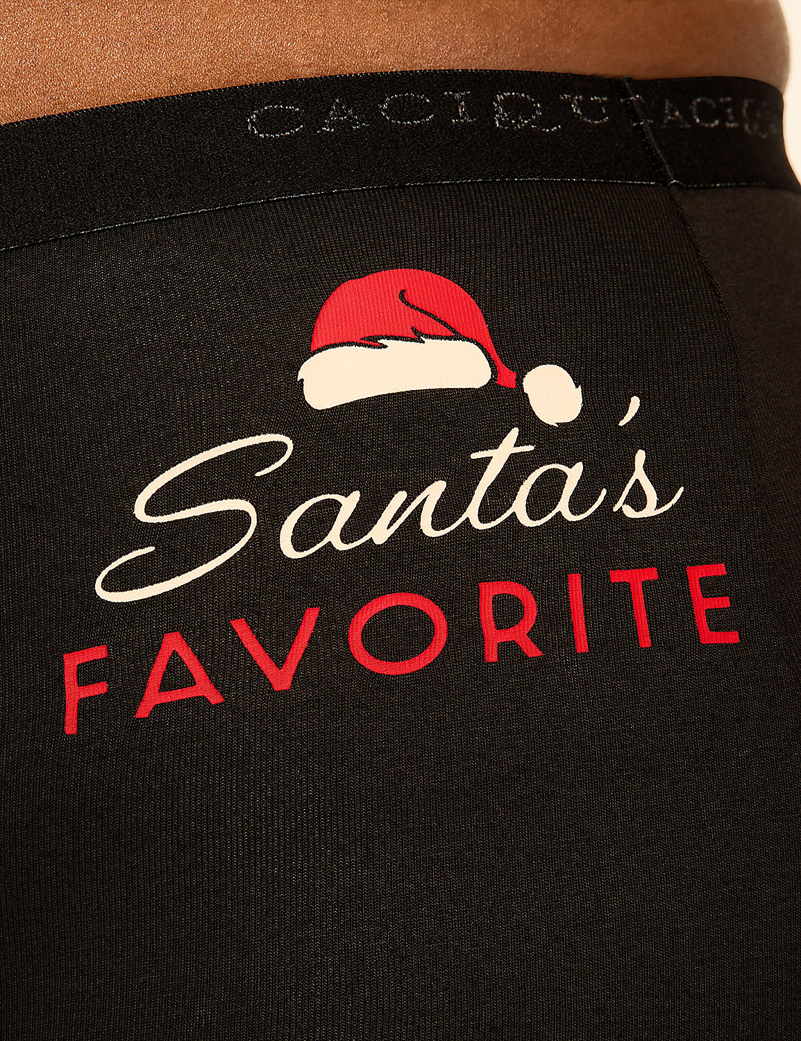 Black fabric with "Santa's Favorite" written in white and red script, topped with a Santa hat, is visible against a blurred background. Product Image 3