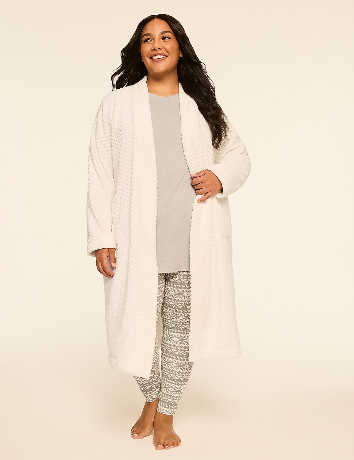 A smiling woman stands in the foreground wearing a white robe over a grey shirt and patterned leggings, against a plain, light-colored background. Product Image 3