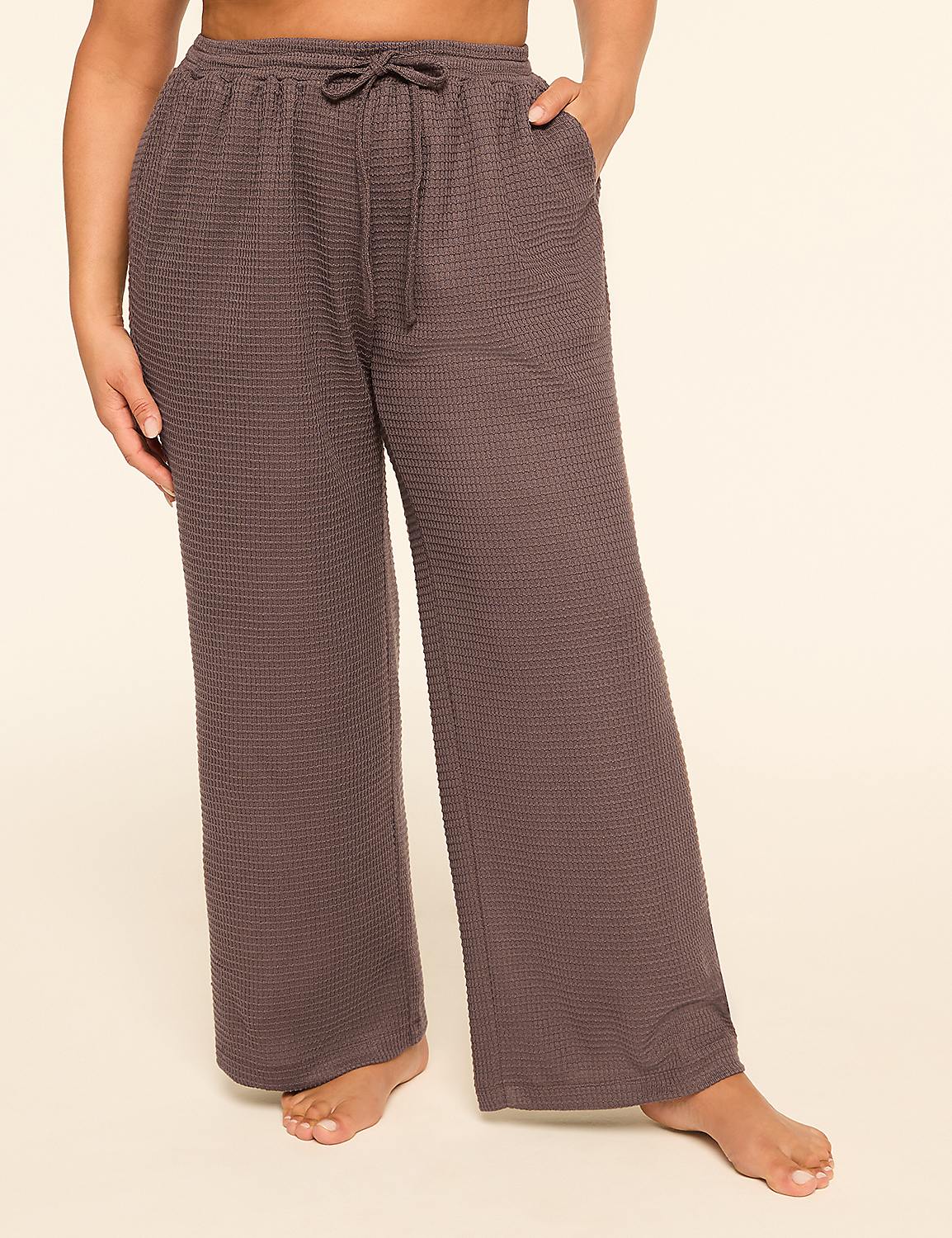 A person stands in the foreground wearing loose-fitting, waffle-knit, charcoal-colored pajama pants with a drawstring, against a plain, light beige background. Product Image 1