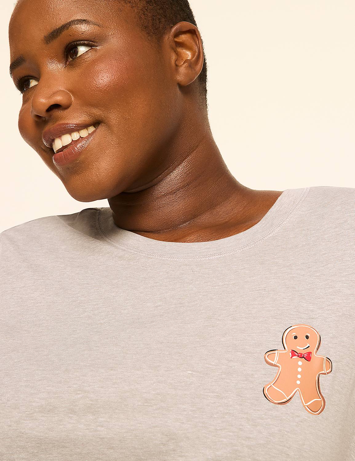 A smiling woman in a light gray shirt with a gingerbread man patch on the chest is shown against a plain, light background. Product Image 4