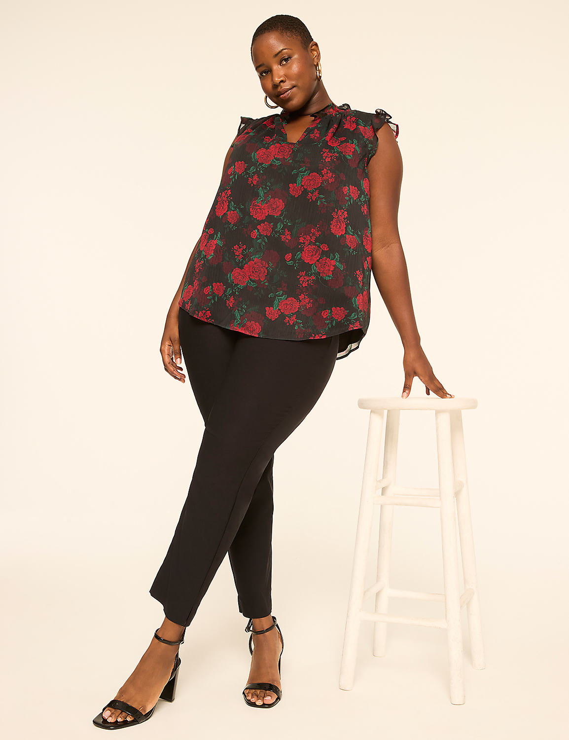 A woman in a floral top and black pants poses next to a stool against a plain background. Product Image 3
