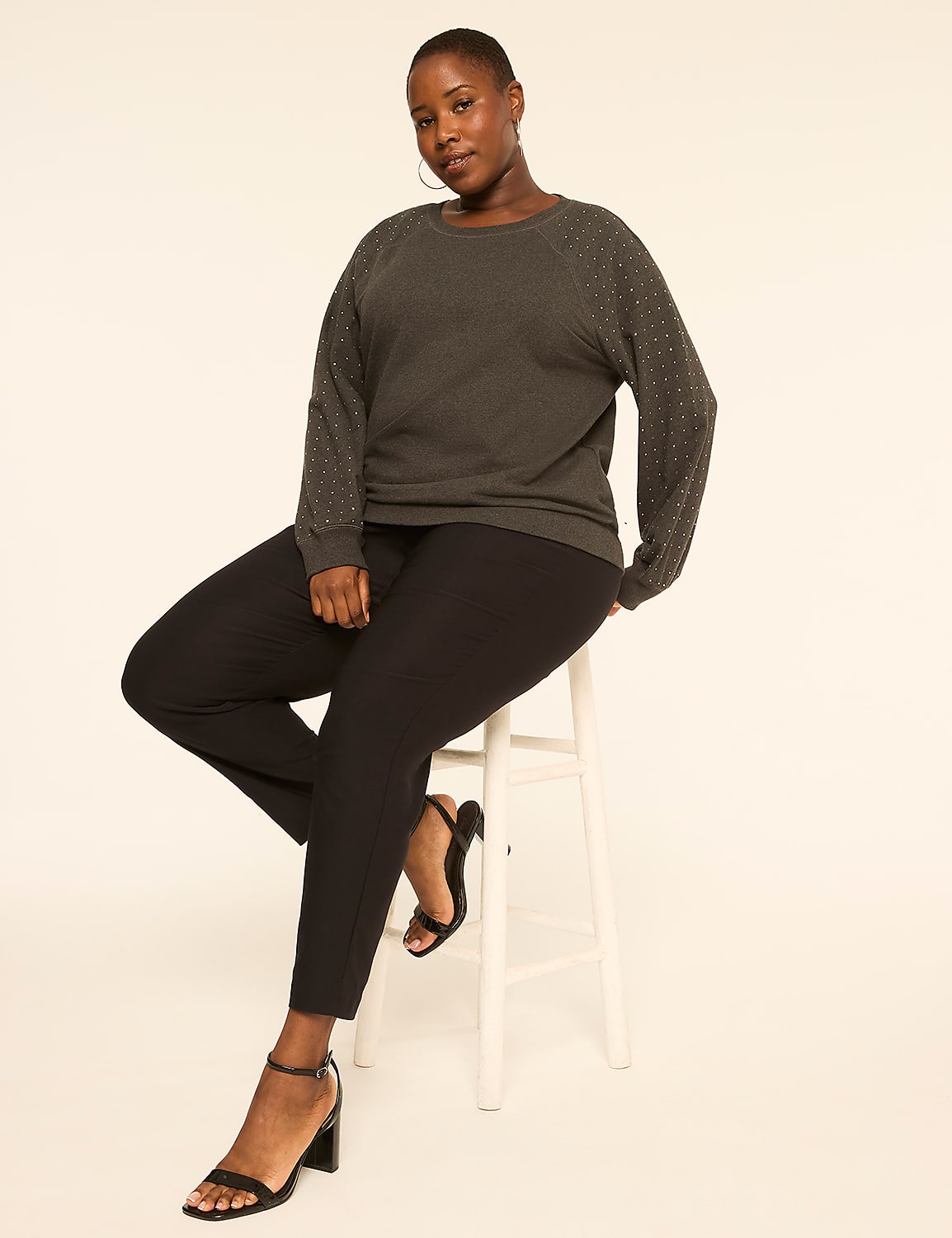 A woman in a dark grey sweater and black pants sits on a white stool against a plain, light background. Product Image 3