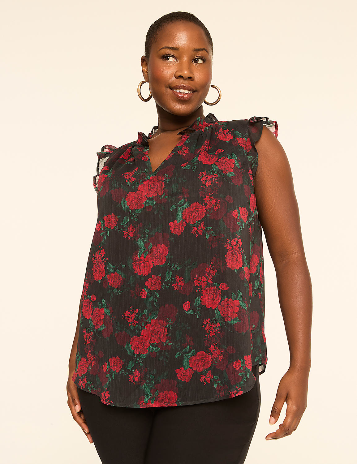 A woman with dark skin and short hair smiles while wearing a black floral top with ruffled sleeves, set against a plain beige background. Product Image 1