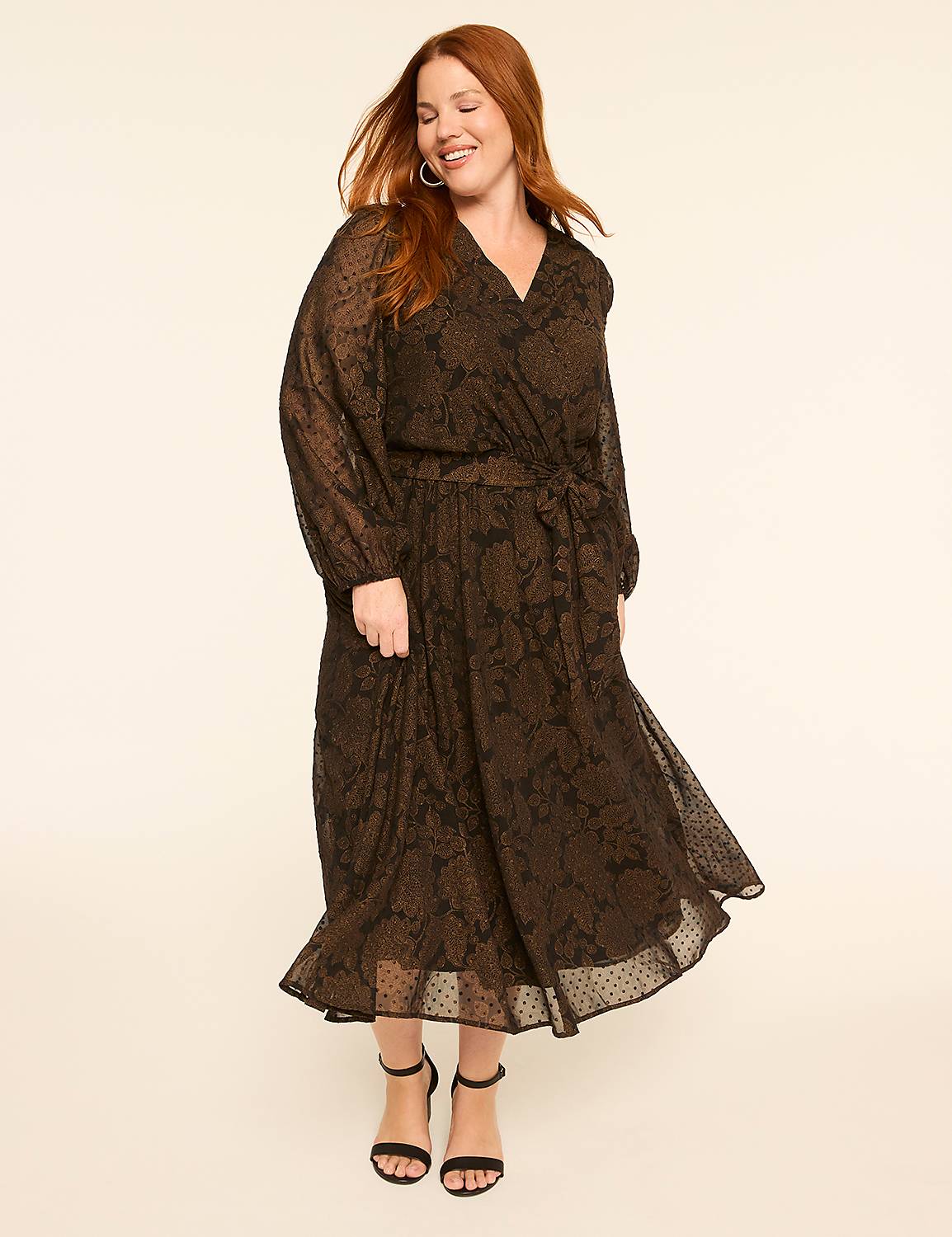 A smiling woman with red hair in a long, patterned black dress stands against a plain, light-colored background. Product Image 1
