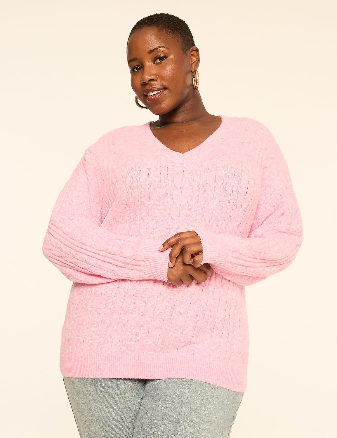A woman in a pink cable-knit sweater stands against a plain, light-colored background. Product Image 1